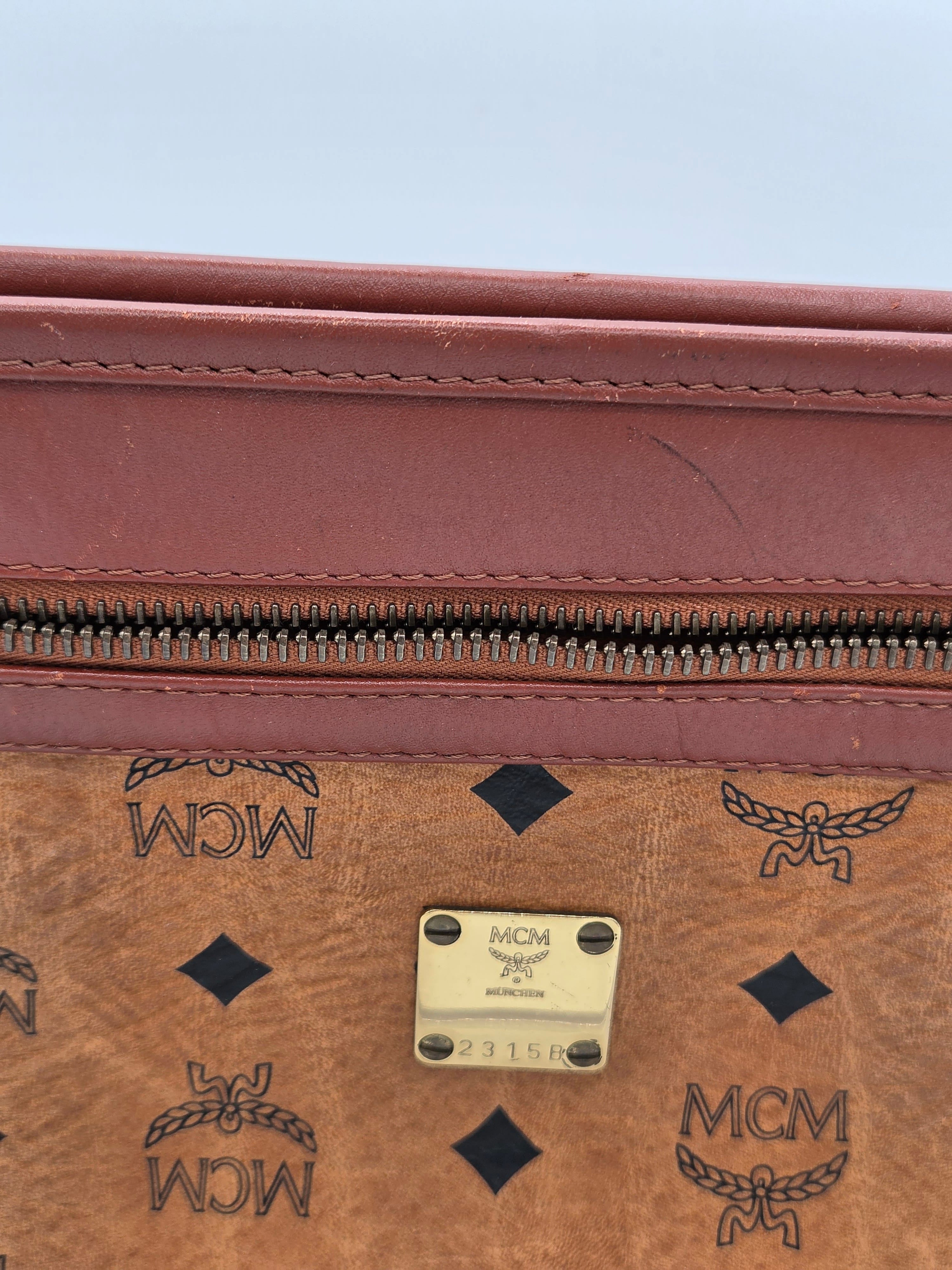 Close-up of an MCM monogram canvas bag in brown with a reddish-brown leather trim and a gold-tone metal plaque.