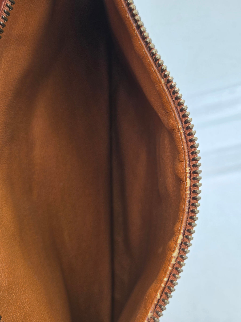 Close-up of the interior opening of a brown leather pouch or clutch, showing the tan leather lining and a metallic zipper along the top edge.