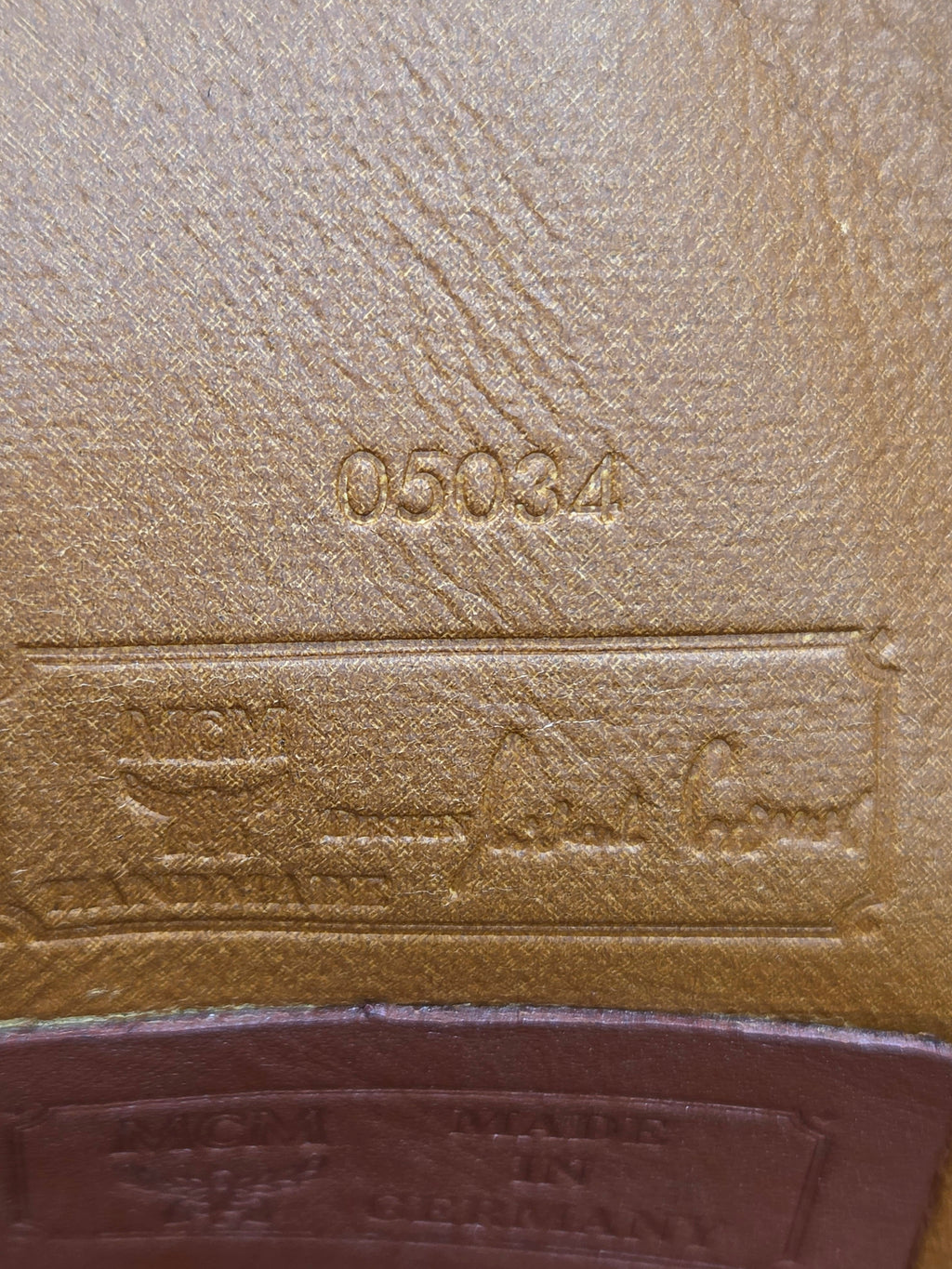 Close-up of a tan textured leather interior with embossed stamped markings including the number 05034 and a rectangular label area with script and logo text.