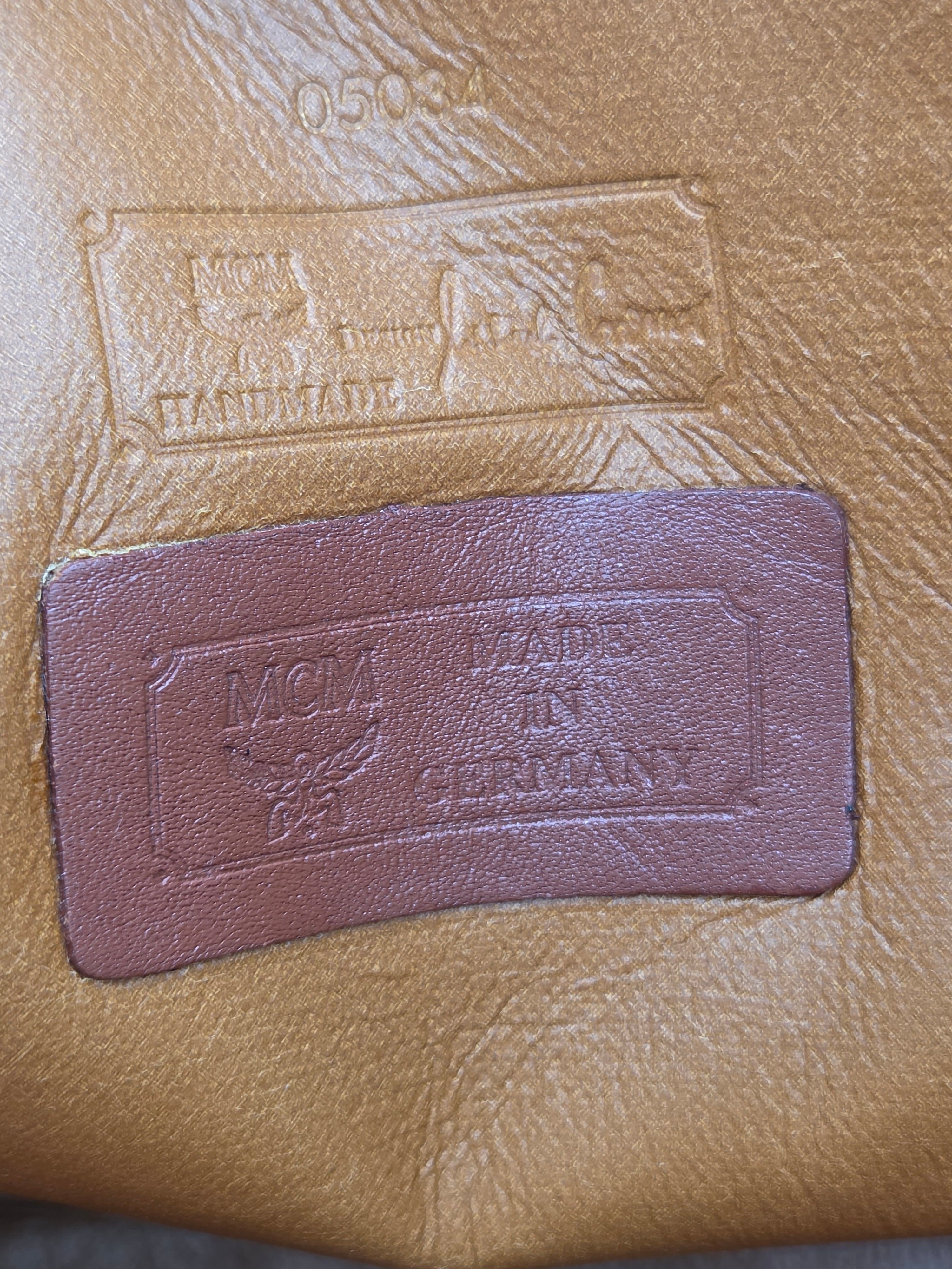 A close-up of a tan leather surface with an embossed rectangular patch and a smaller sewn brown leather brand patch reading 'Vogue' and 'Gentleman' with a floral emblem.