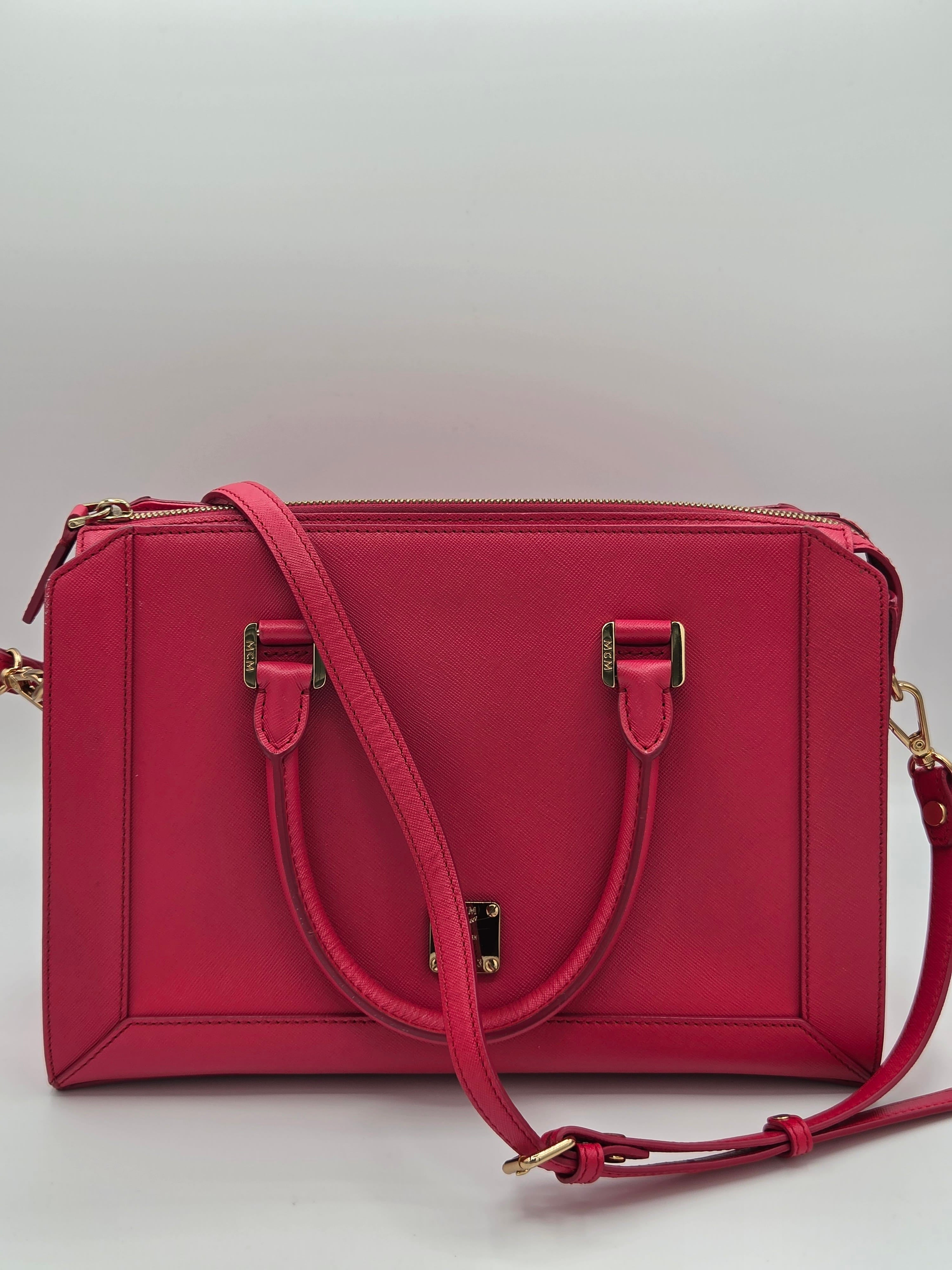 A structured rectangular handbag in a rich magenta pink leather, featuring a top zipper, a matching top handle, a detachable shoulder strap, and gold-tone hardware.
