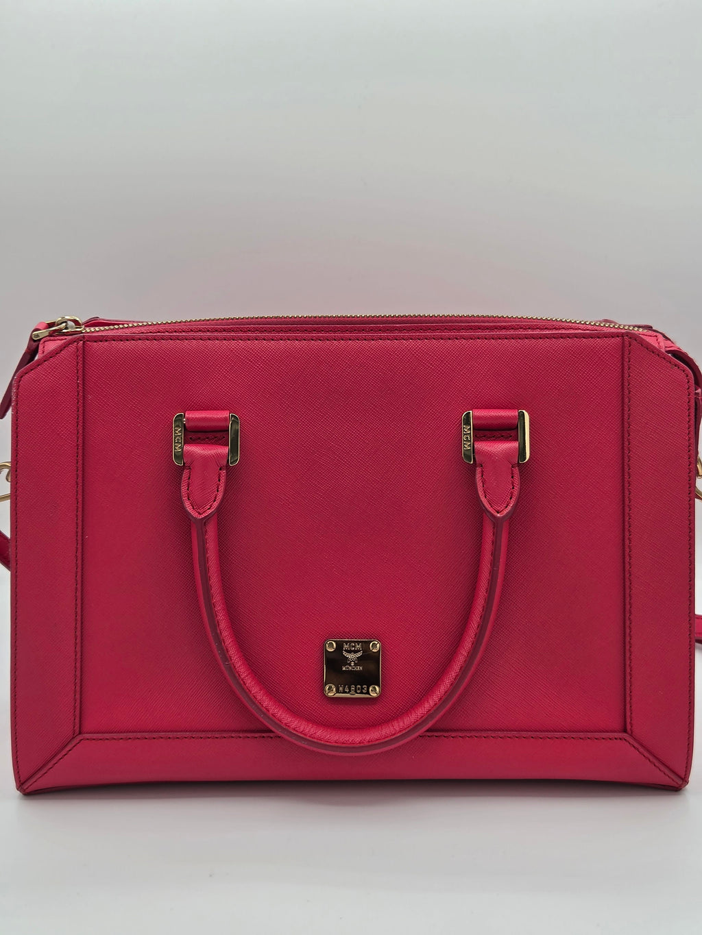 A structured red leather handbag with double top handles, gold-tone hardware, and a zip-around closure, shown from a top-down view on a light gray background.