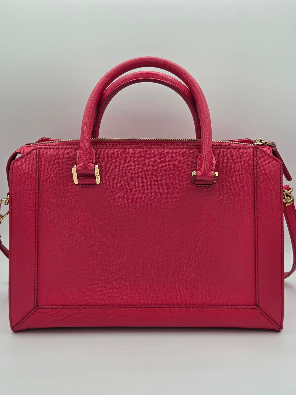 A structured rectangular handbag in deep red leather with double top handles, gold-tone hardware, and a shoulder strap, shown from a top-down view on a light gray background.