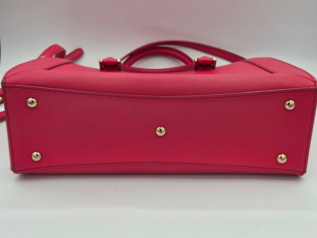 A bright pink textured leather handbag shown from the bottom, featuring gold-tone metal studs and a top handle, on a white background.