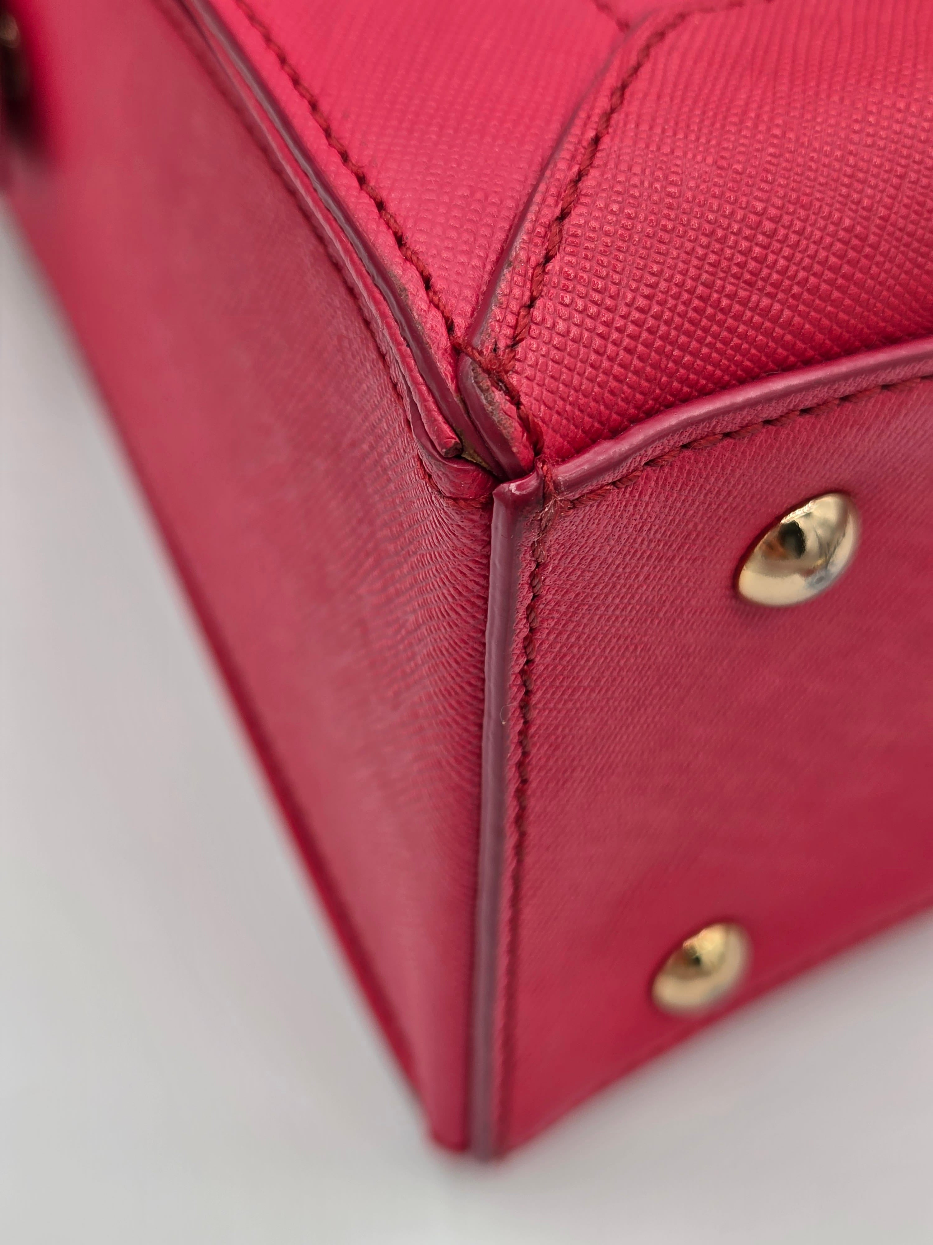 Close-up detail of a textured pink handbag corner showing gold-tone metal studs and stitching on a white background.