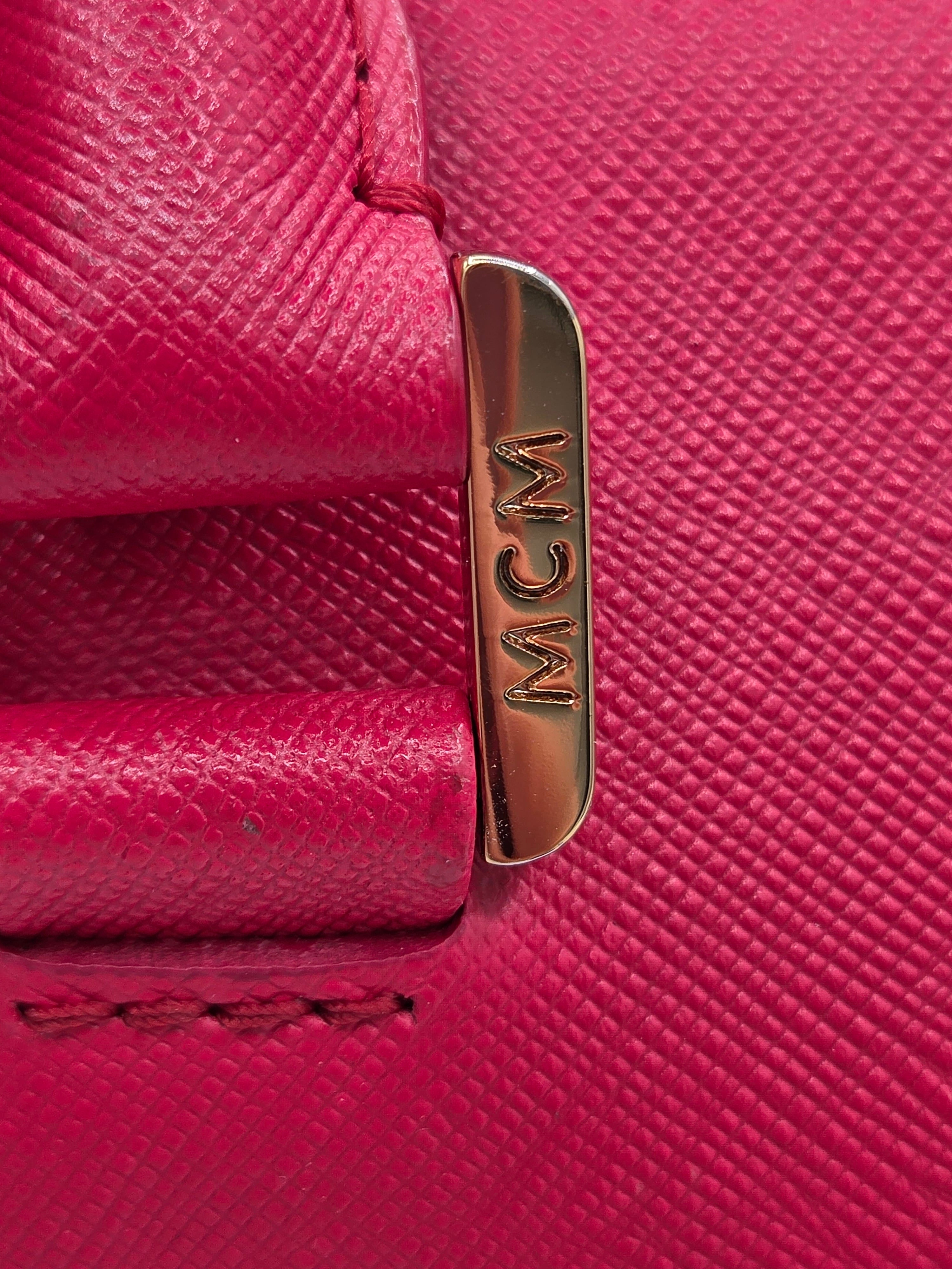 Close-up of a textured pink leather accessory with a polished gold-tone metal clasp engraved with the letters 'MCM'.
