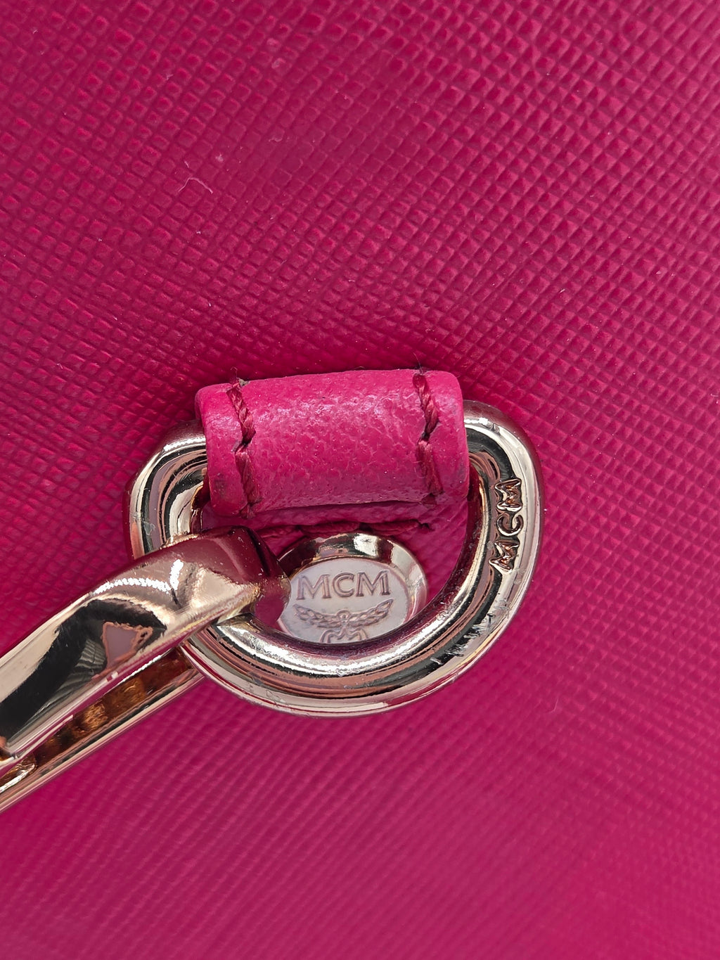 Close-up of an MCM handbag featuring a vibrant pink textured leather strap with a matching pink leather loop and polished gold-tone metal hardware.