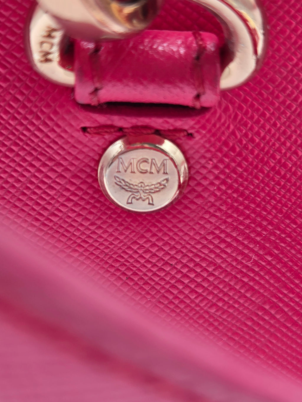 Close-up of a textured hot pink leather handbag with a silver-tone metal ring and an embossed MCM logo on a round metal tag.