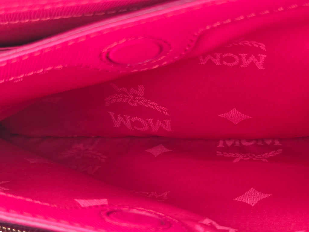 Close-up of a bright pink MCM wallet or clutch showing the interior lining with embossed MCM logos and diamond motifs.