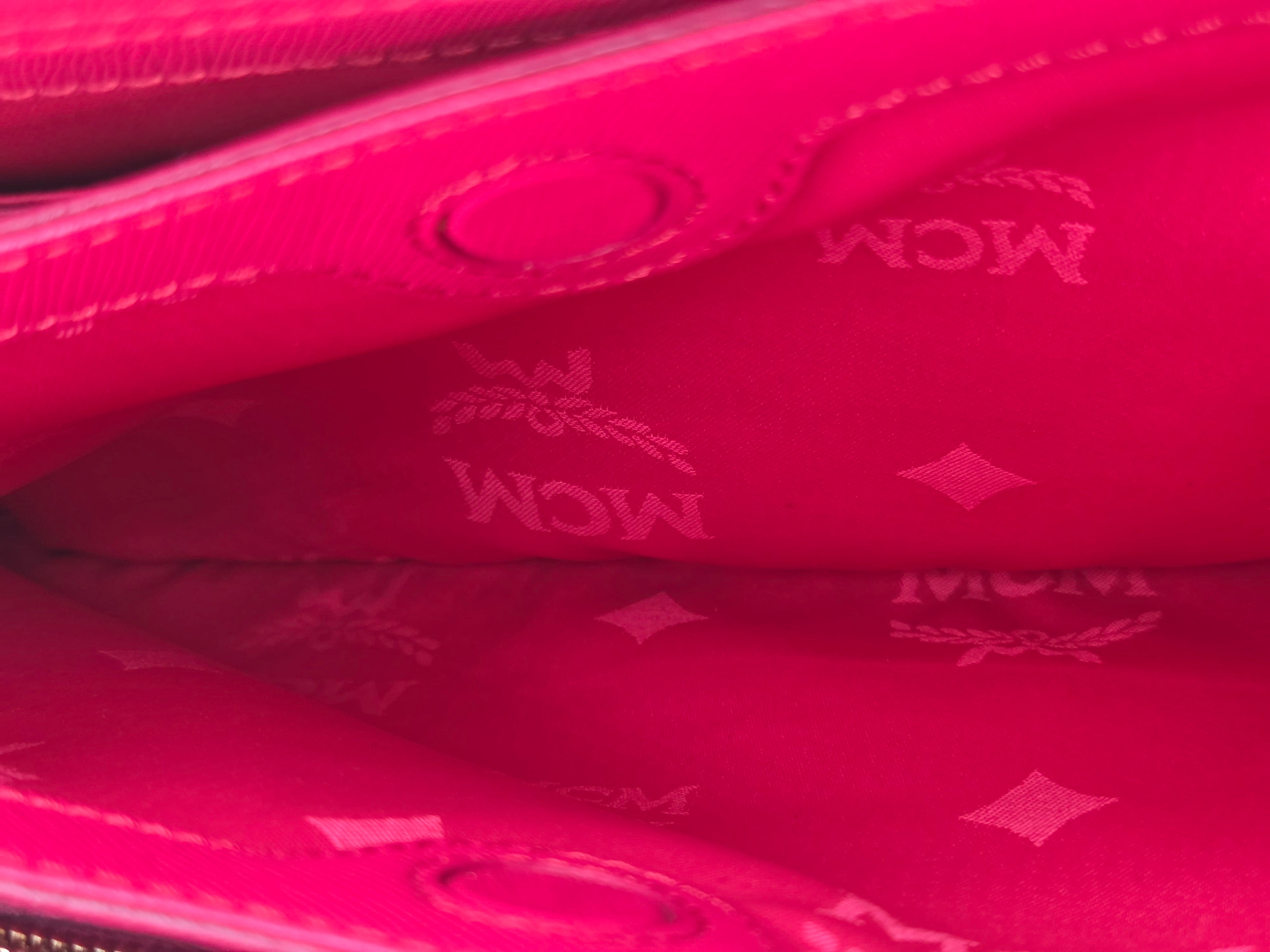 Close-up of a bright pink MCM wallet or clutch showing the interior lining with embossed MCM logos and diamond motifs.