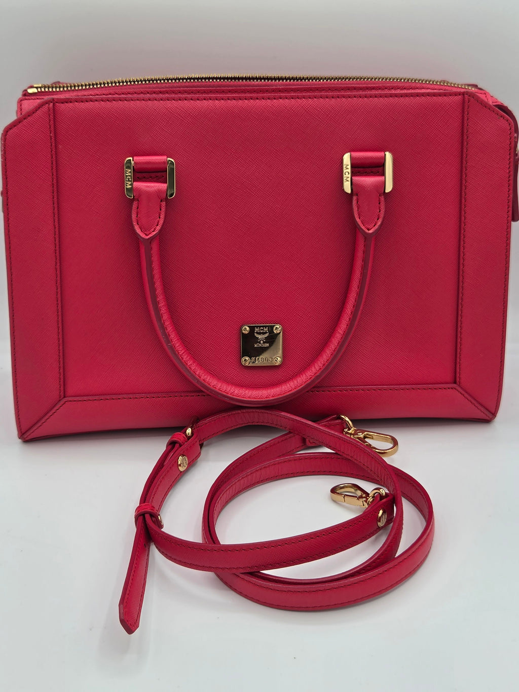 A structured red leather handbag with a top handle, gold-tone hardware, and an additional detachable shoulder strap, photographed on a plain light background.