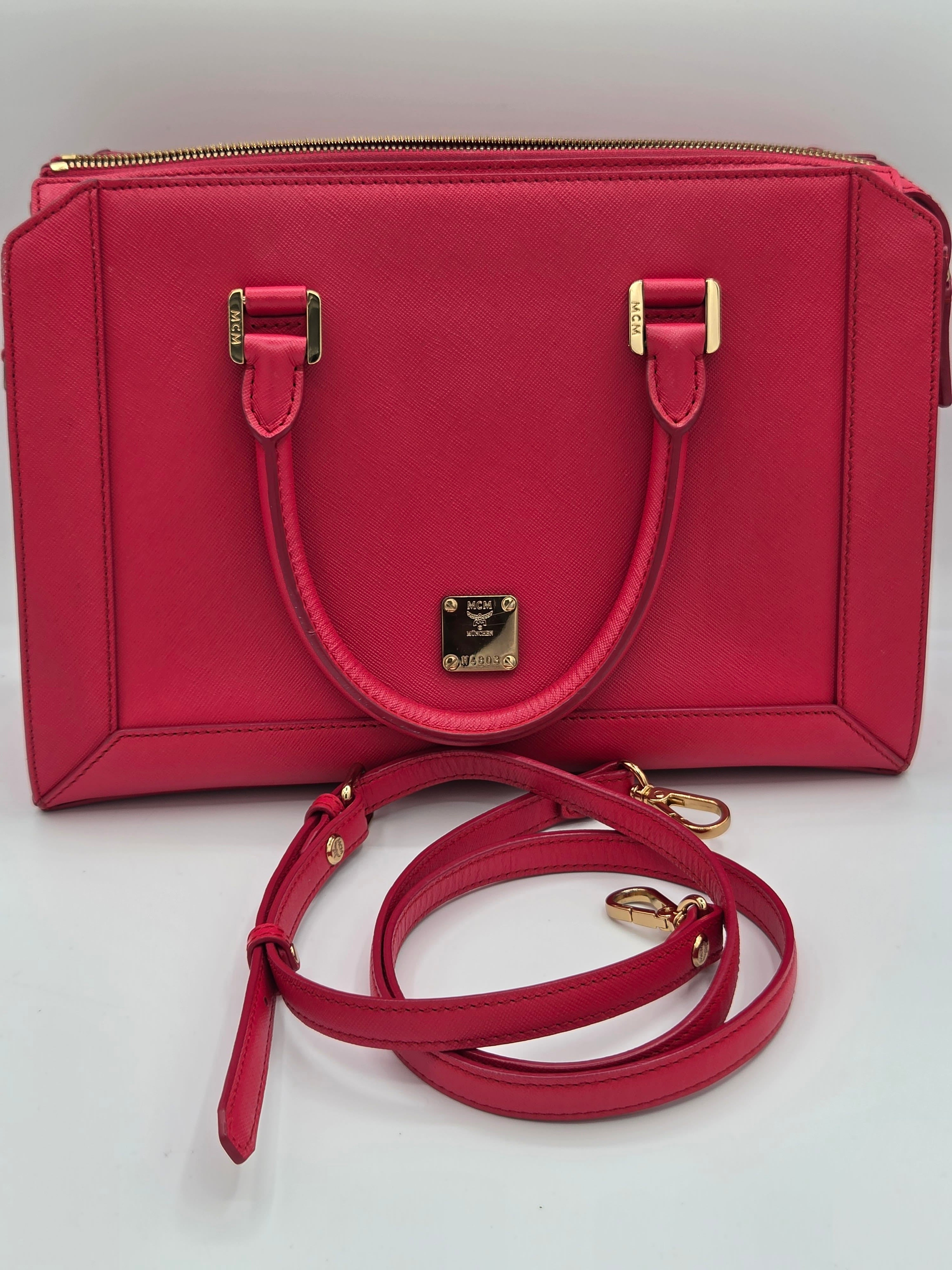 A structured red leather handbag with a top handle, gold-tone hardware, and an additional detachable shoulder strap, photographed on a plain light background.