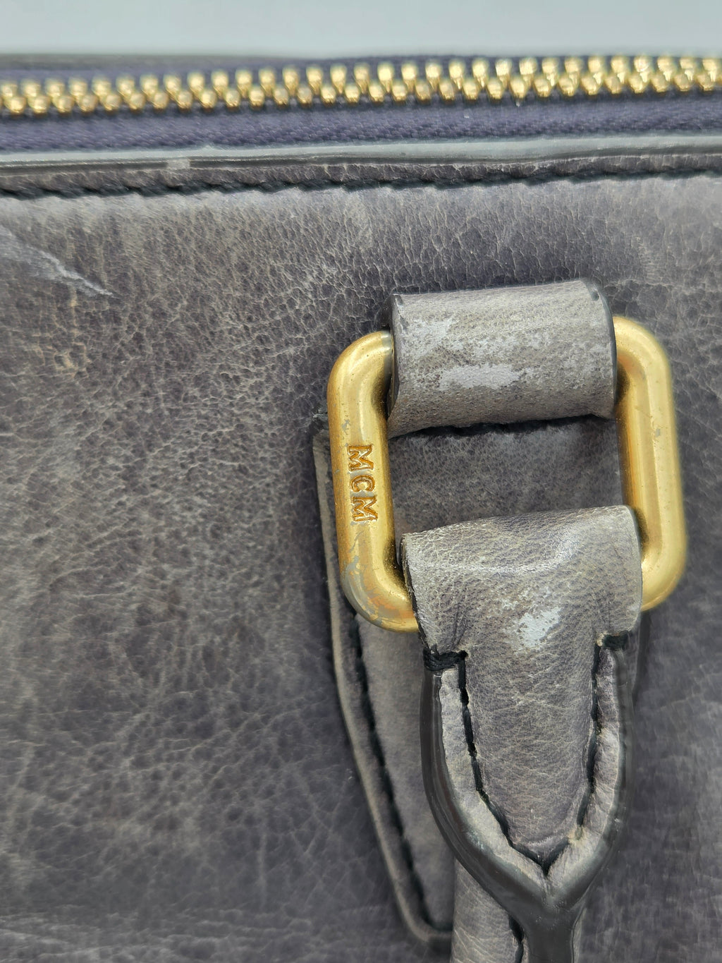 Close-up of a distressed gray leather bag with a gold-tone metal D-ring and zipper pull.