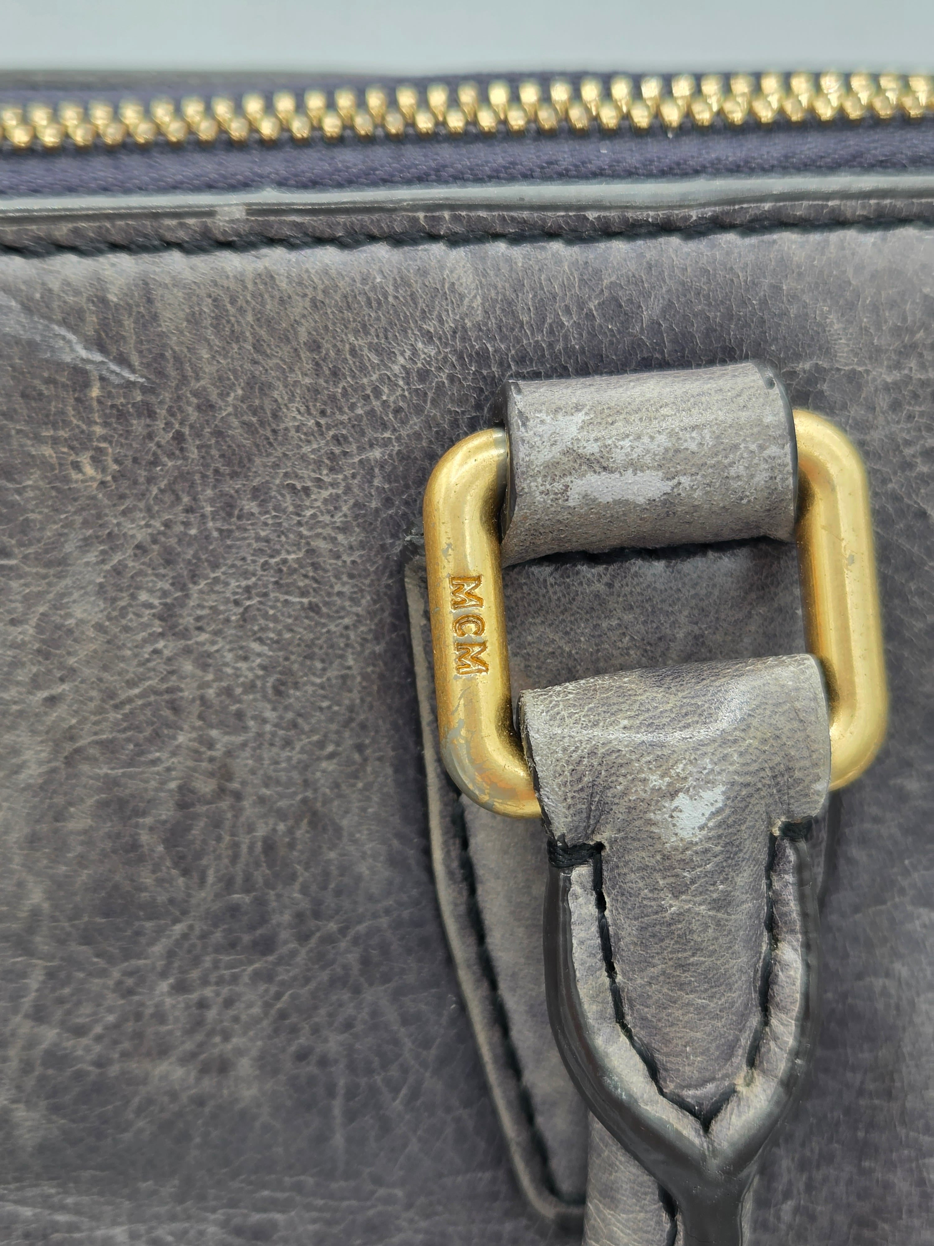 Close-up of a distressed gray leather bag with a gold-tone metal D-ring and zipper pull.