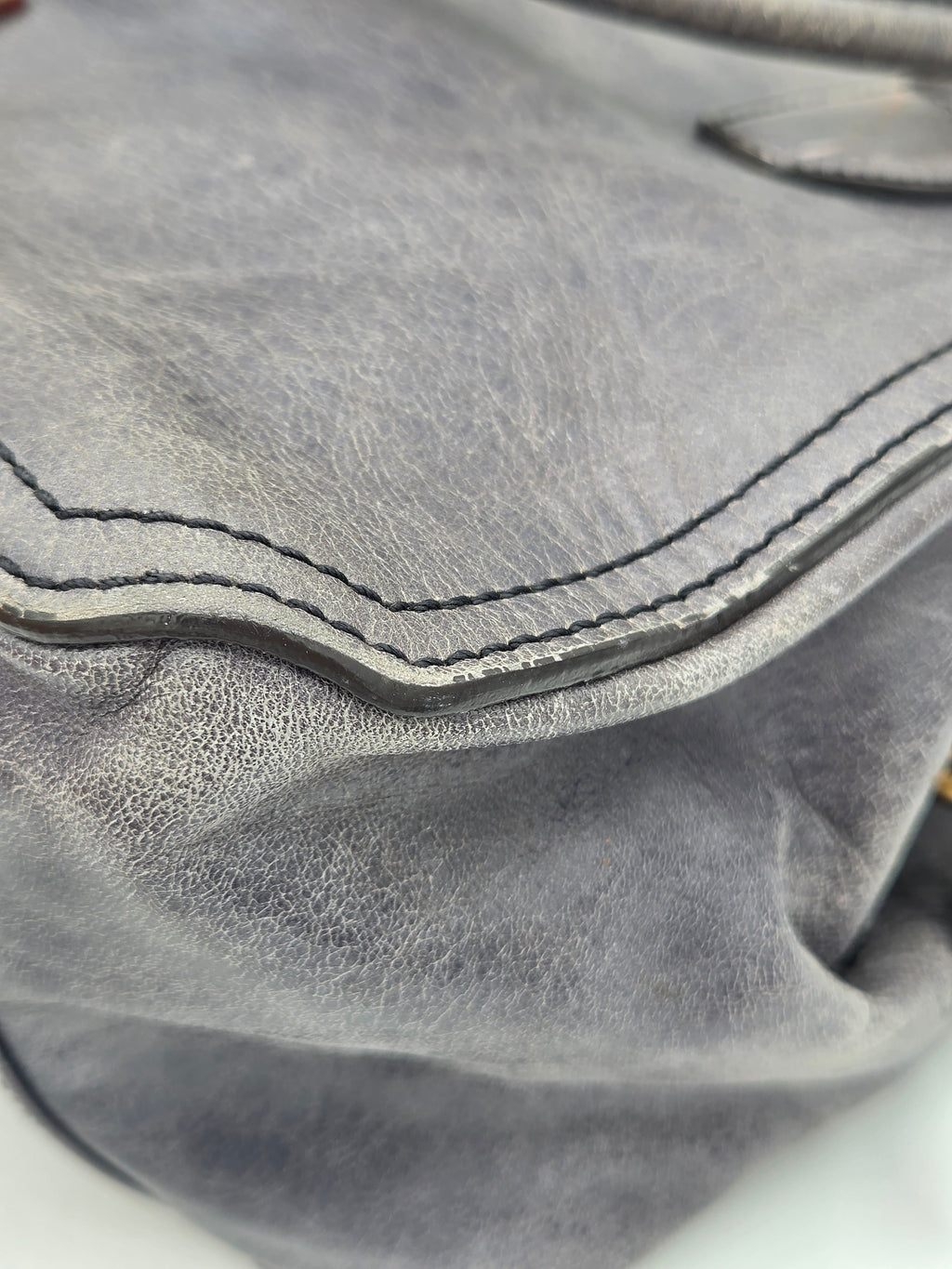 Close-up of a gray leather bag showing the texture of the leather and the contrast stitching along a curved edge.