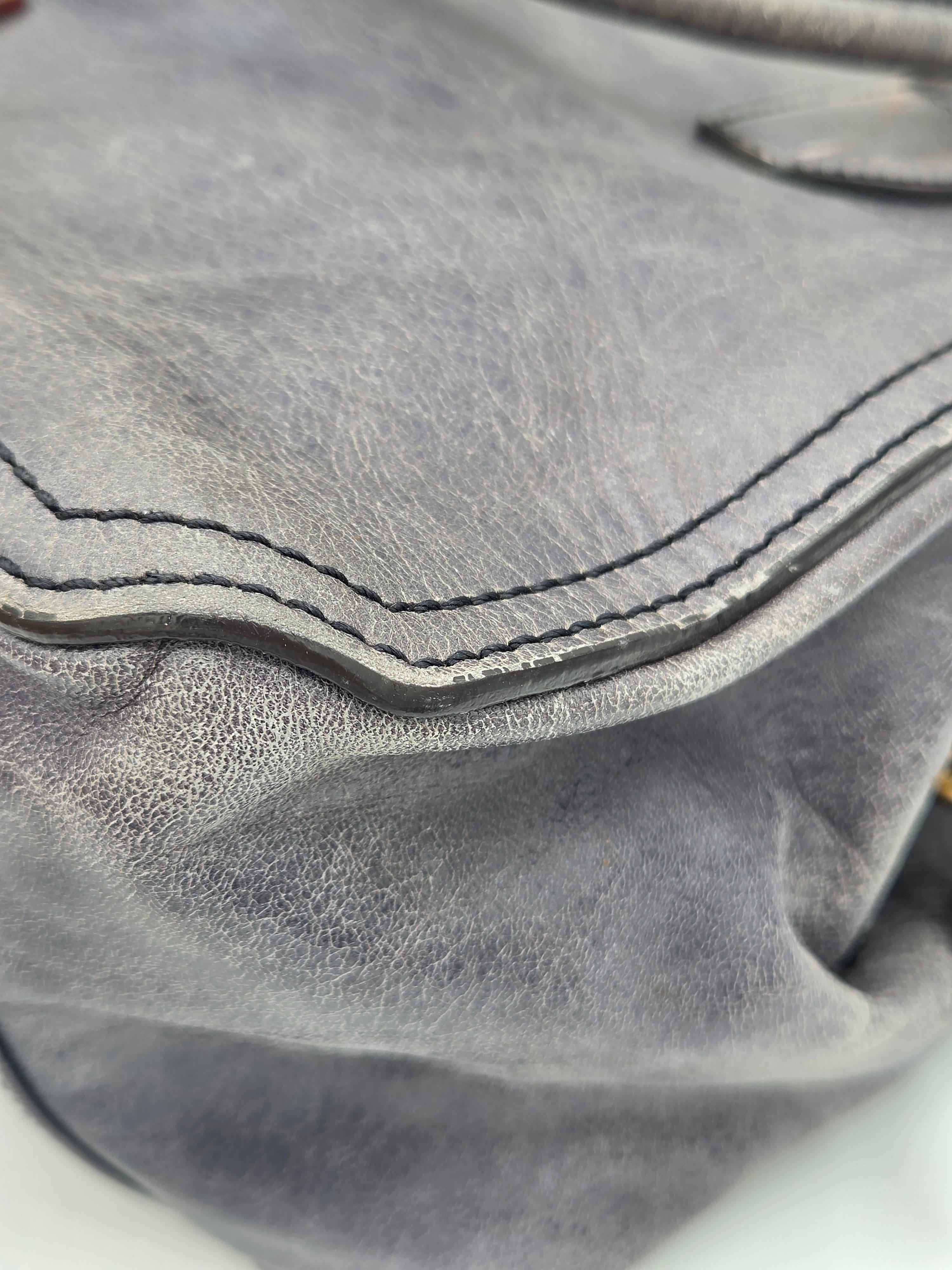 Close-up of a gray leather bag showing the texture of the leather and the contrast stitching along a curved edge.