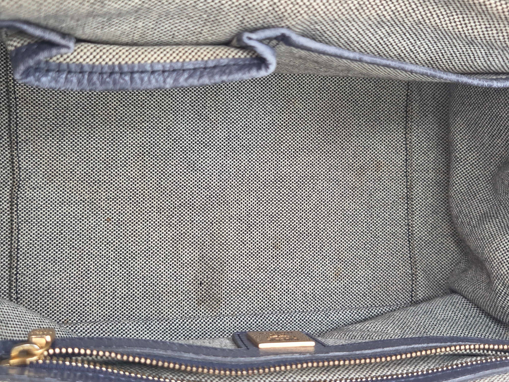 Close-up of the interior of a textured gray fabric bag, showing a zippered compartment with a gold-tone zipper pull and a blue-gray stitched trim.
