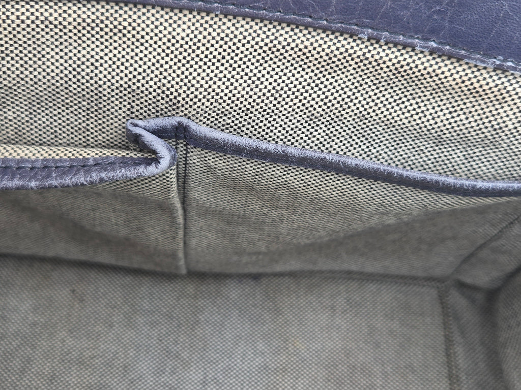 Close-up of the interior fabric lining of a bag or case, showing a woven olive green material with dark gray stitched edges and a small pocket opening.