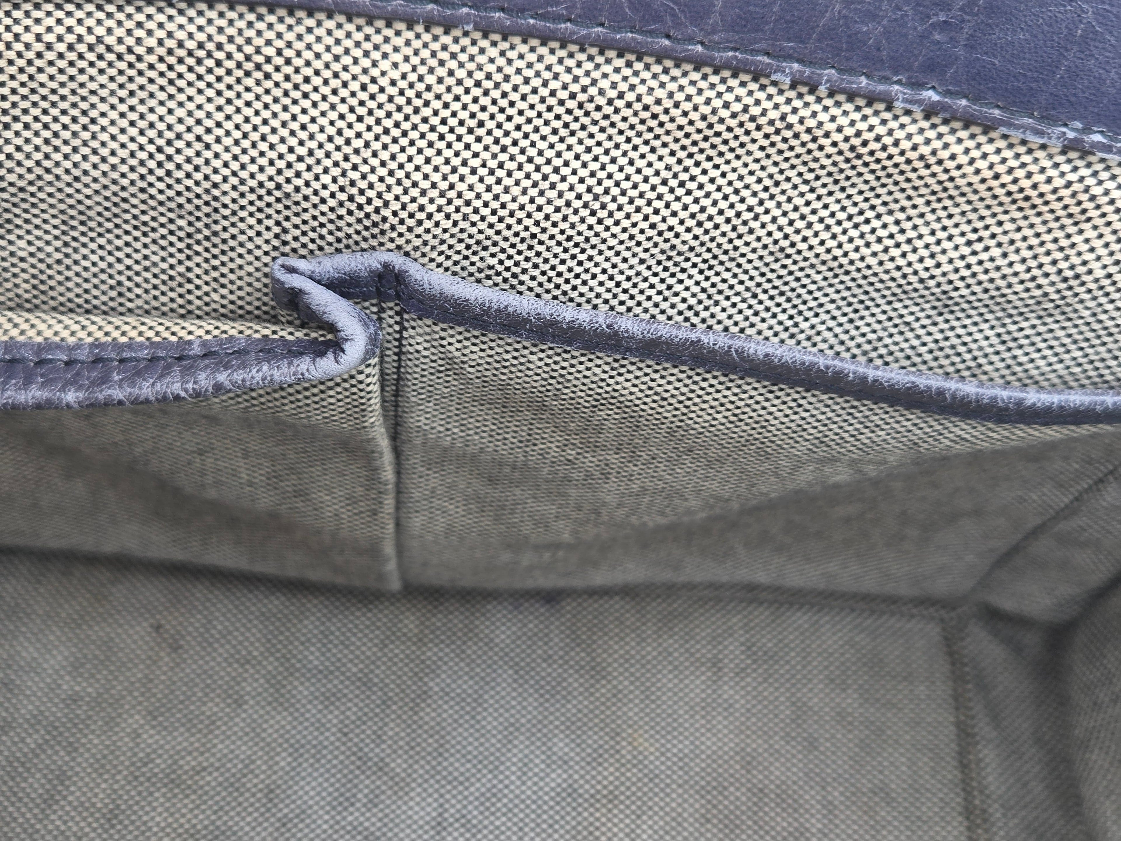 Close-up of the interior fabric lining of a bag or case, showing a woven olive green material with dark gray stitched edges and a small pocket opening.