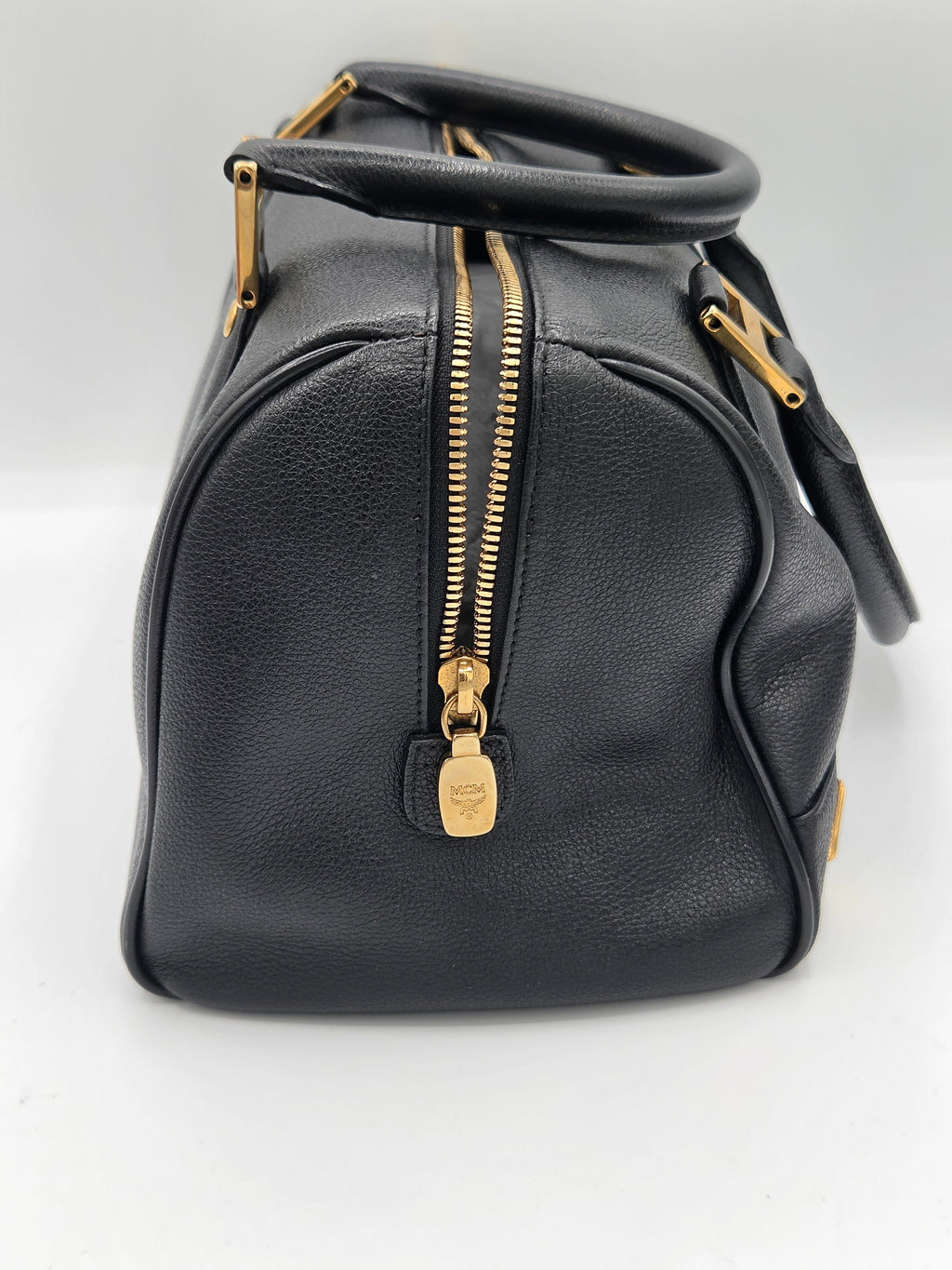 A black pebbled leather handbag with gold-tone hardware, featuring a top zipper, a top handle, and a shoulder strap, photographed on a plain white background.