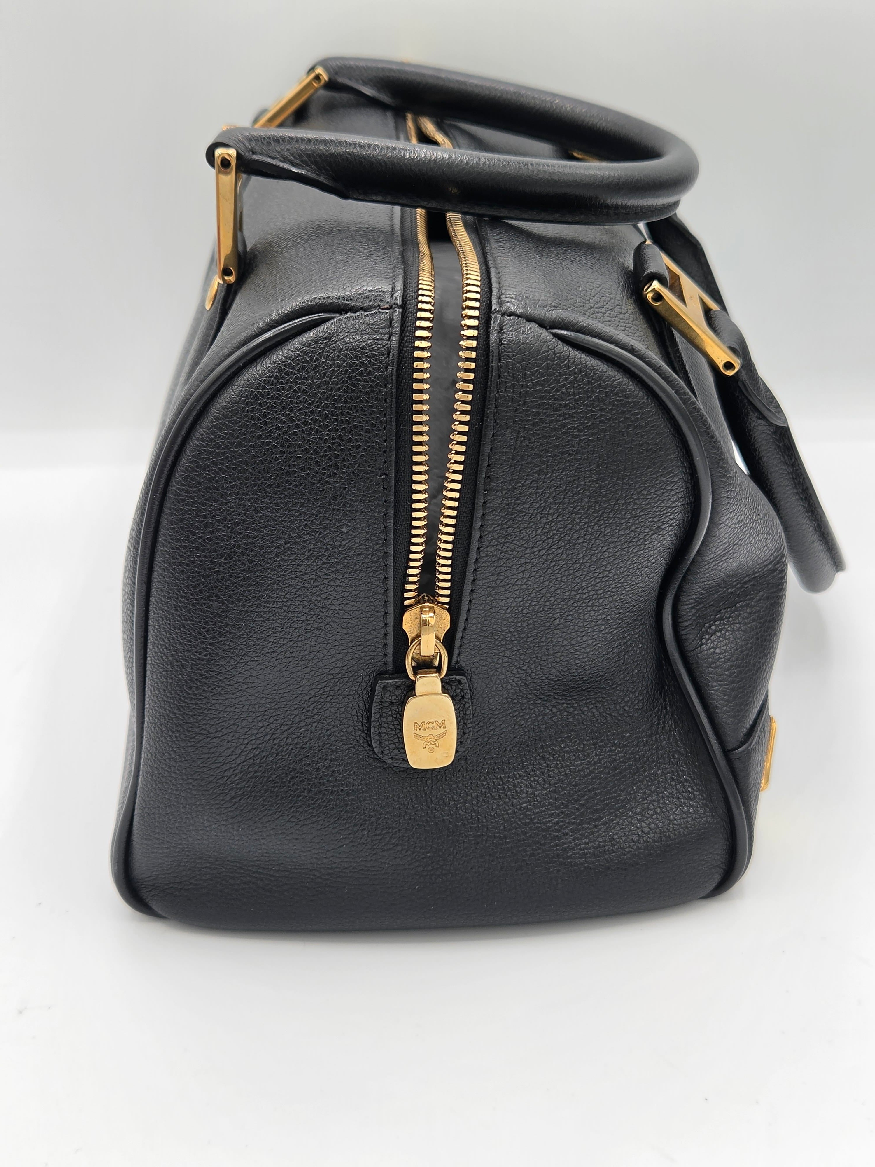 A black pebbled leather handbag with gold-tone hardware, featuring a top zipper, a top handle, and a shoulder strap, photographed on a plain white background.