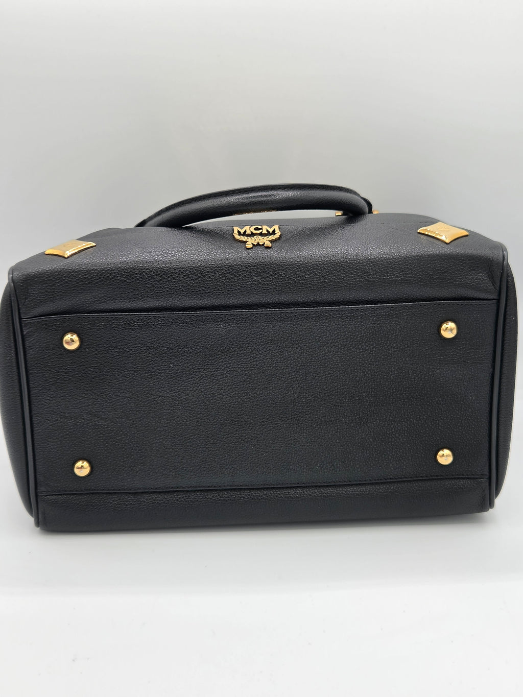 Black textured leather handbag shown from a side angle, featuring gold-tone hardware, diamond-shaped studs, and a small crest logo on the handle against a plain white background.