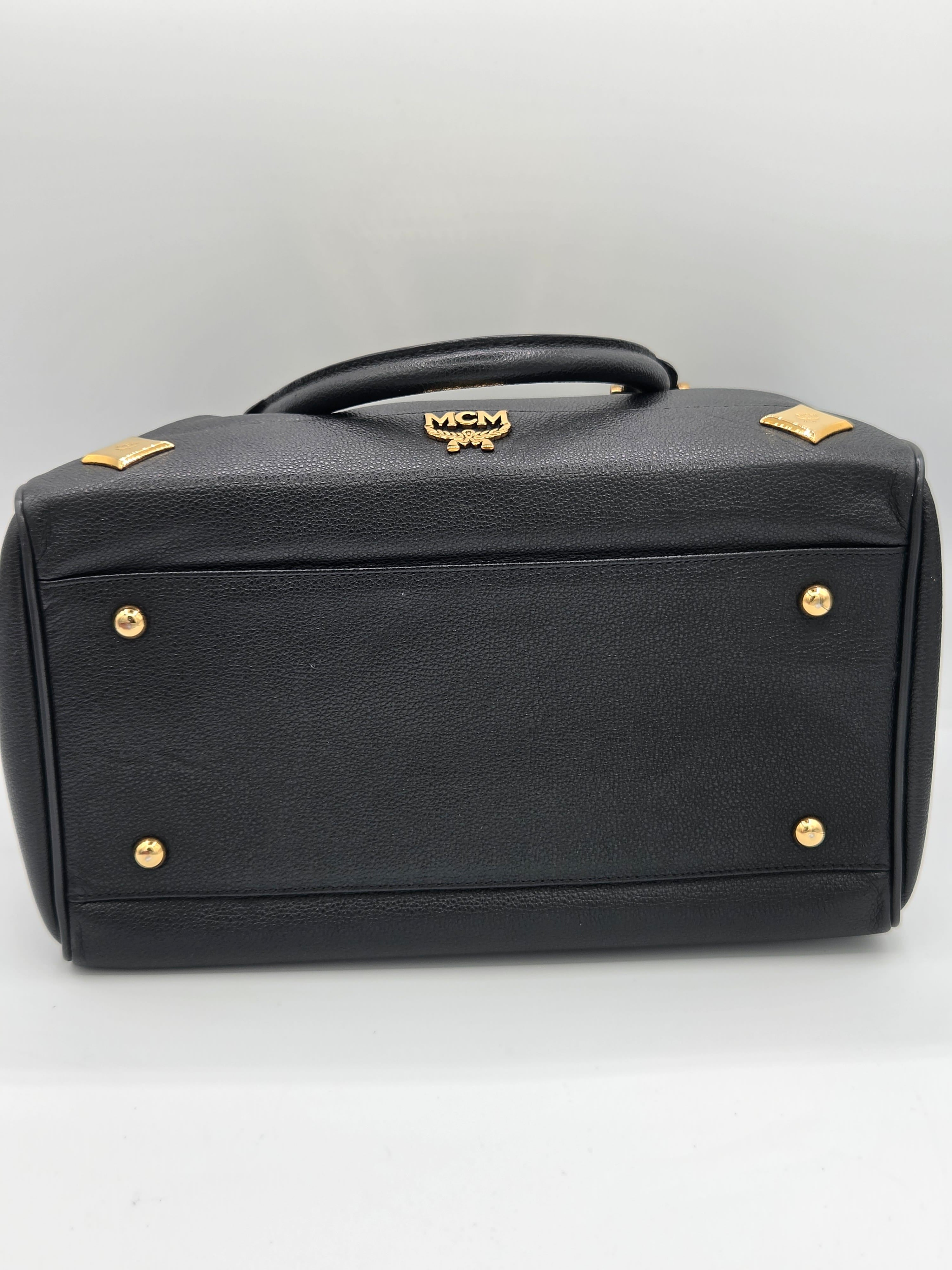 Black textured leather handbag shown from a side angle, featuring gold-tone hardware, diamond-shaped studs, and a small crest logo on the handle against a plain white background.
