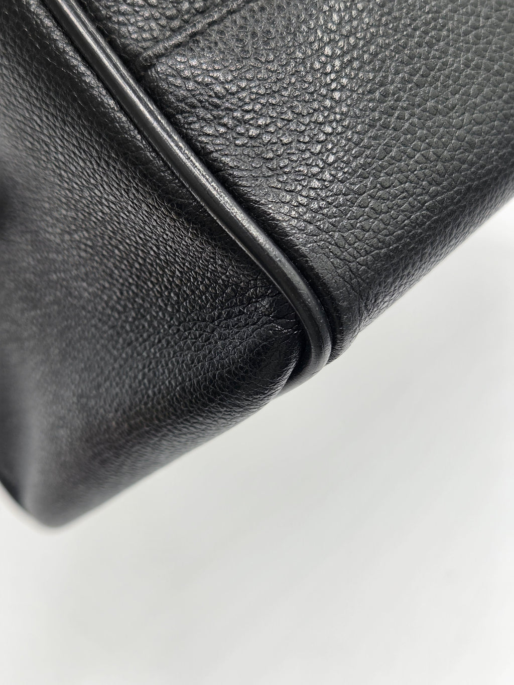 Close-up of a black pebbled leather handbag corner showing the texture and edge stitching against a white background.