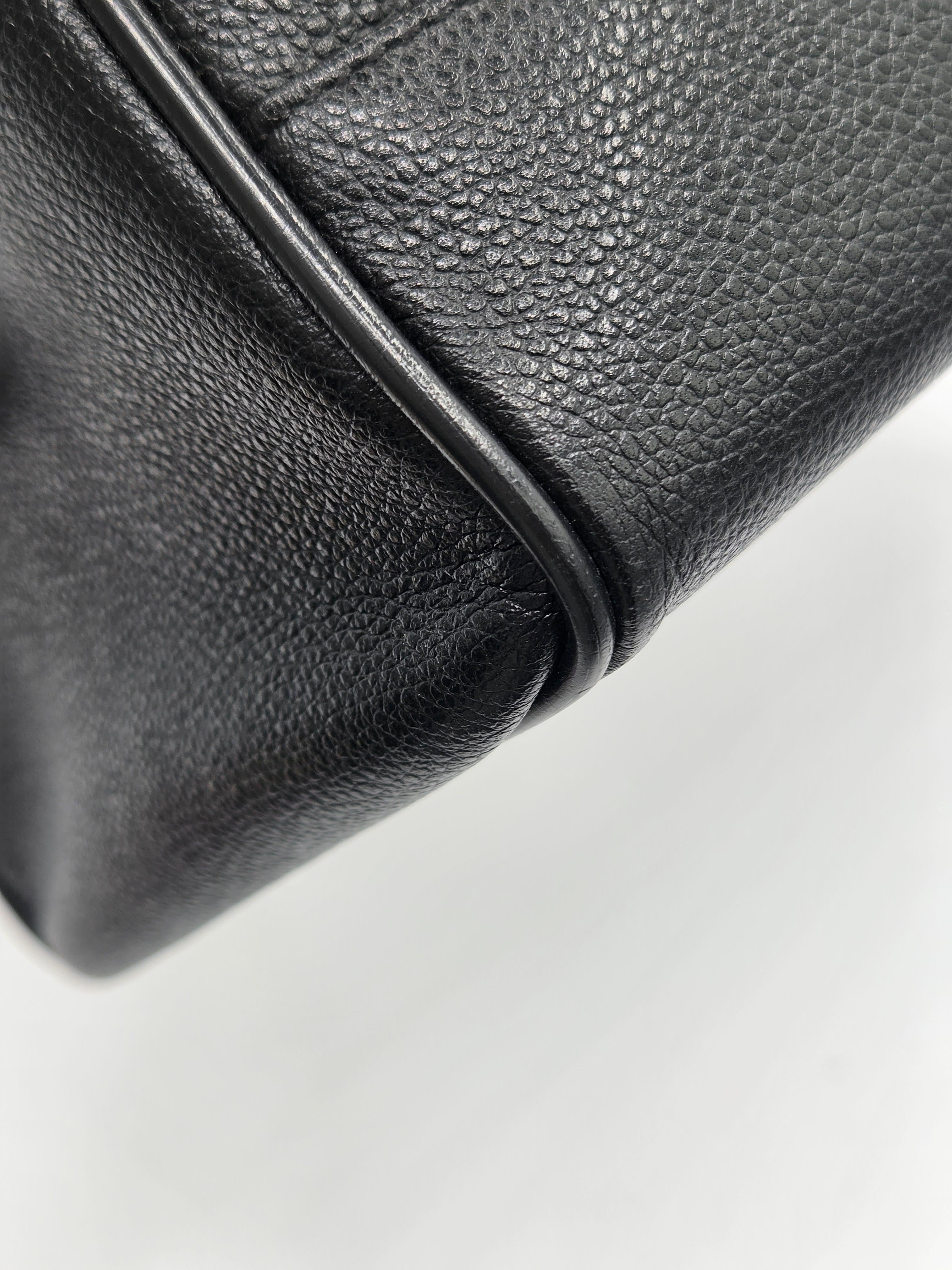 Close-up of a black pebbled leather handbag corner showing the texture and edge stitching against a white background.
