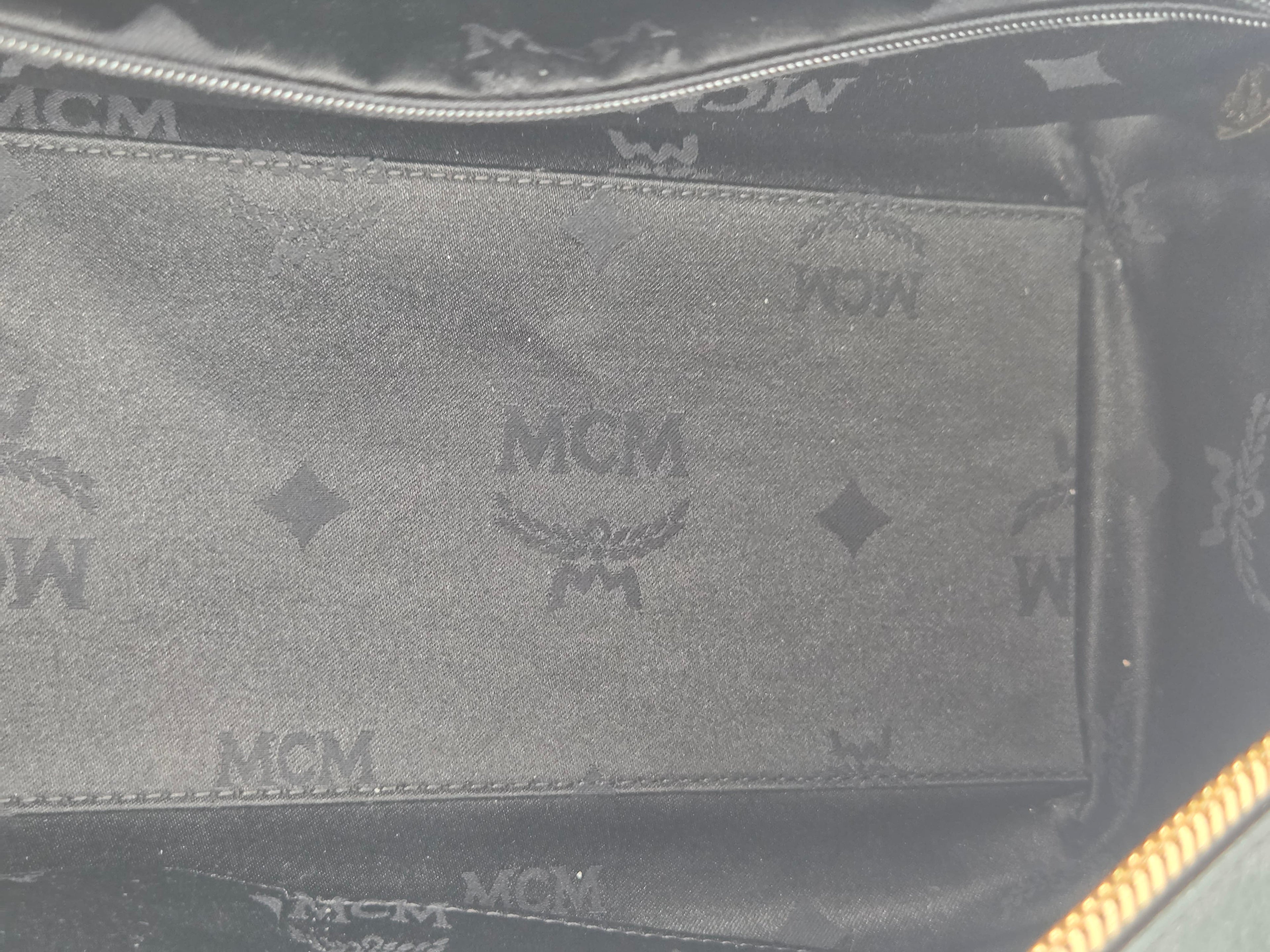 Close-up of the interior lining of a black MCM bag, showing the signature embossed MCM logo and monogram pattern on a dark gray fabric.