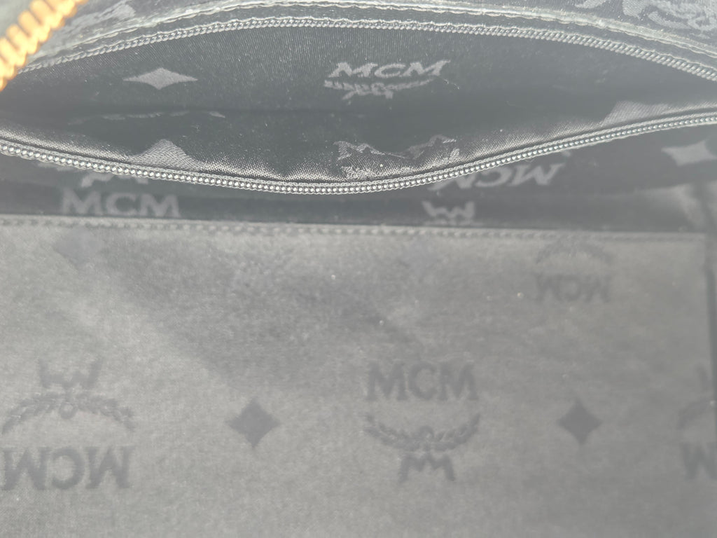 Close-up of the interior lining of an MCM handbag, showing the signature dark gray and black monogram canvas with a silver zipper.