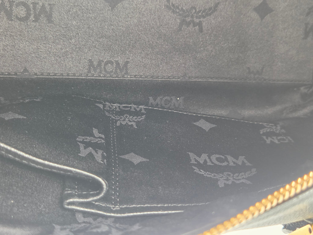 Close-up of the interior lining of a black MCM monogram bag, showing the brand's signature logo pattern and a gold zipper along the top edge.