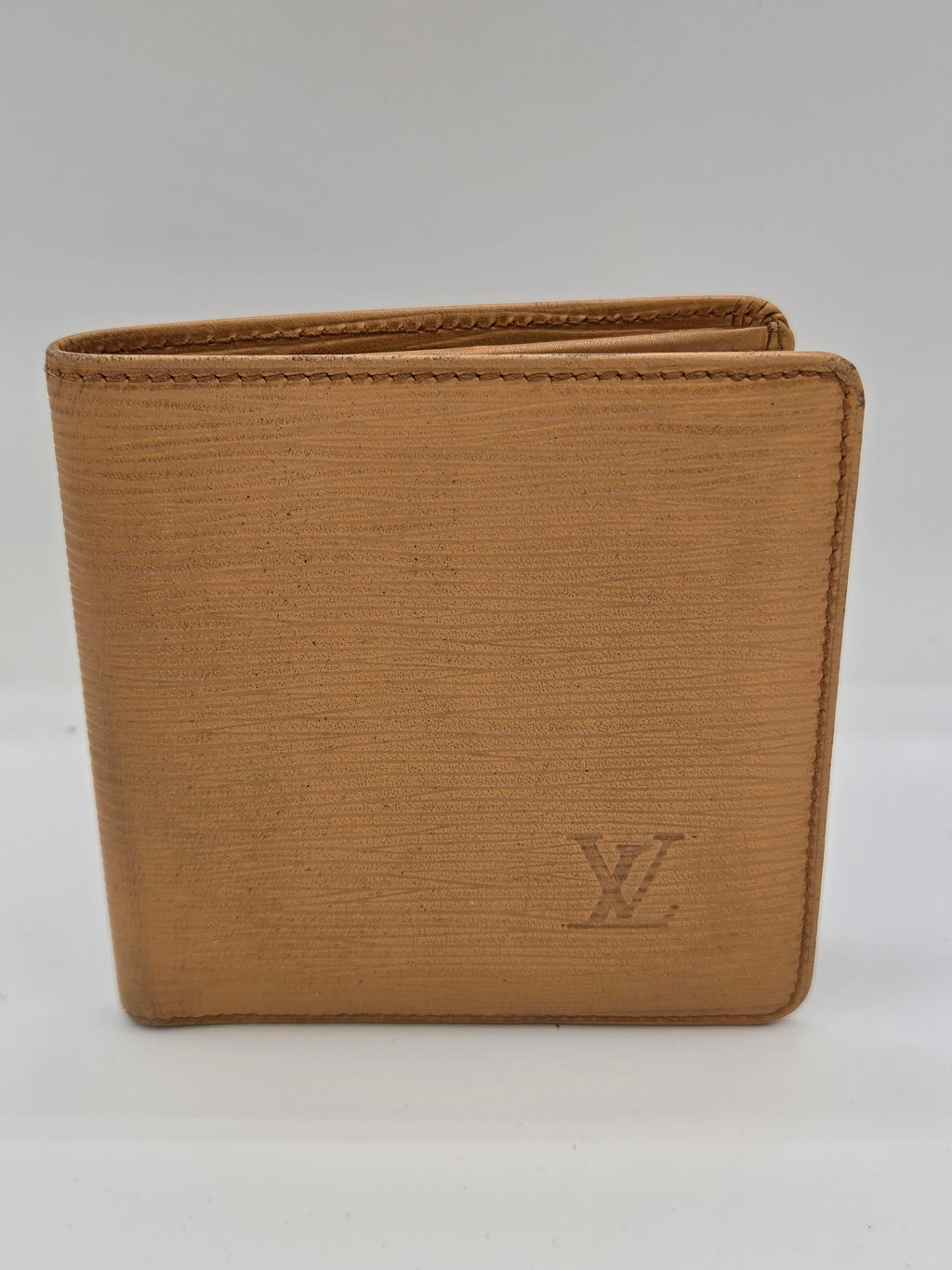 A tan textured leather bifold wallet with an embossed Louis Vuitton LV logo on the front, shown against a plain white background.