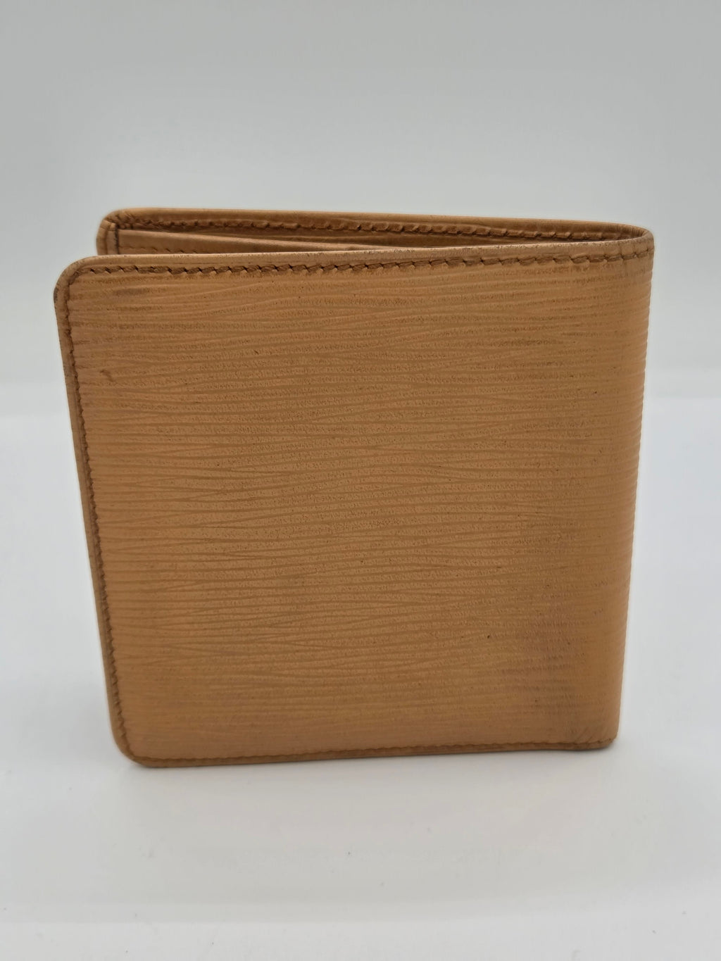 A tan textured leather bi-fold wallet shown closed against a plain white background.