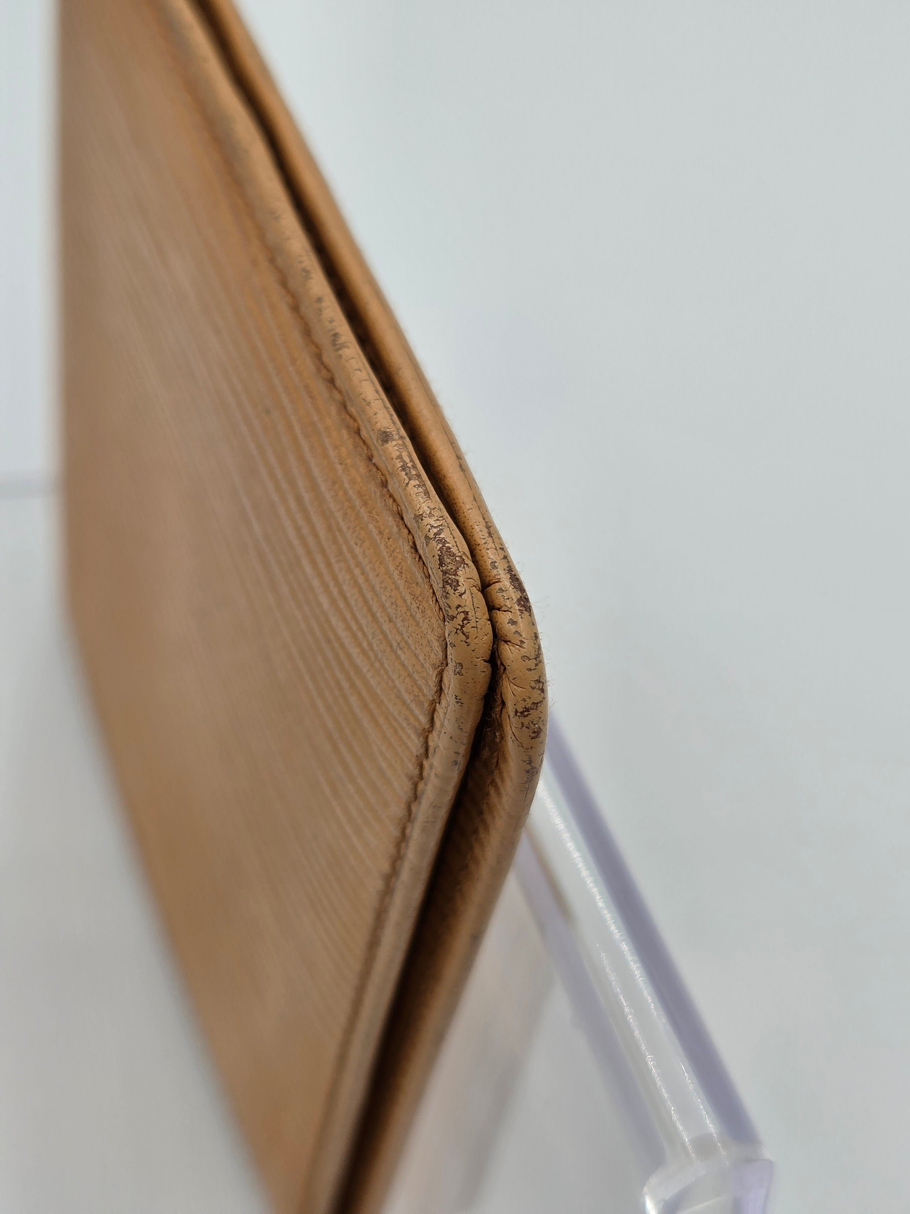 Close-up of a tan leather wallet corner with visible grain texture and a clear plastic straw partially inserted, set against a plain light background.