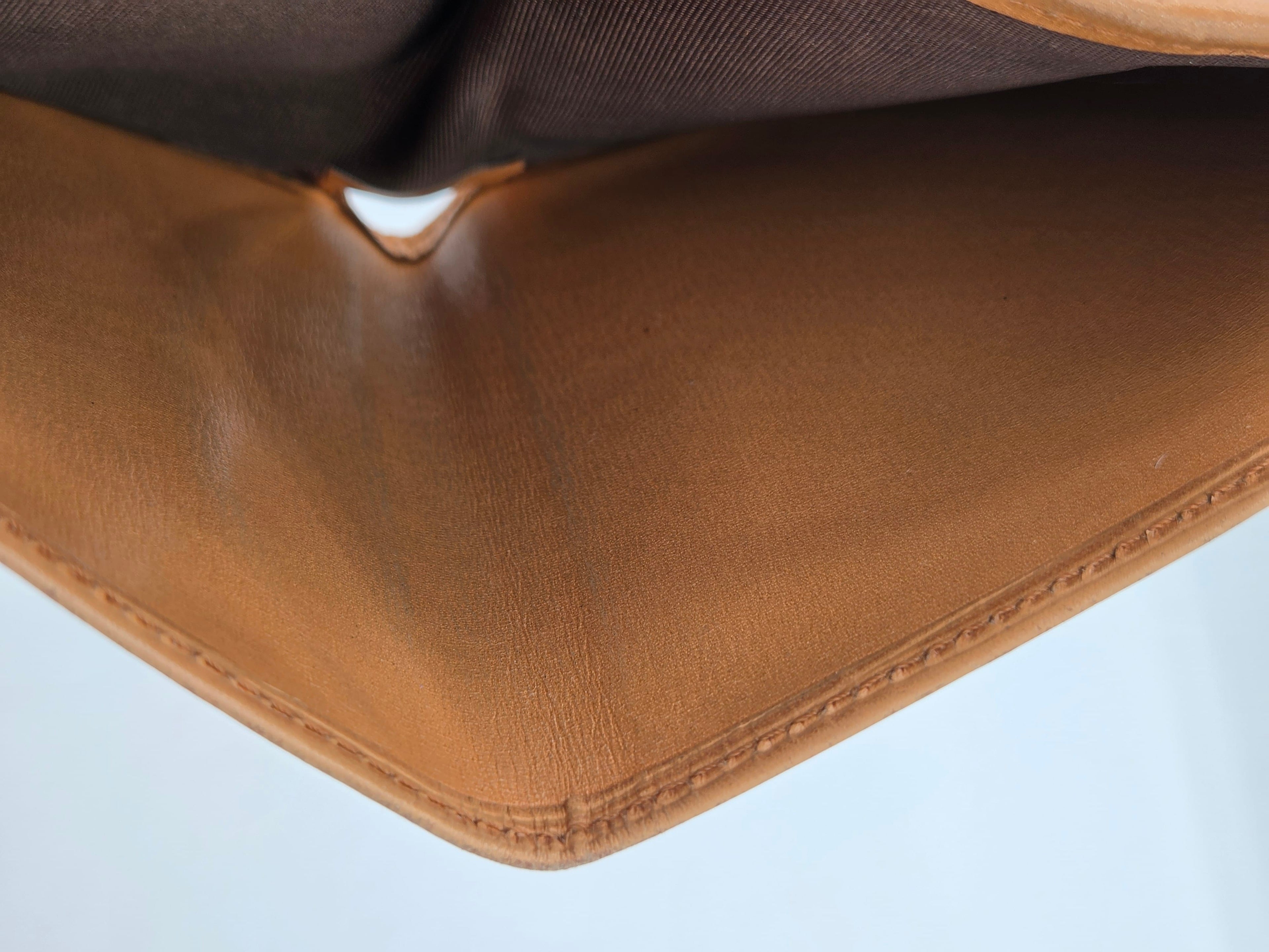 Close-up detail of a tan leather or faux-leather corner with visible stitching and a dark brown fabric interior below, against a pale light blue background.