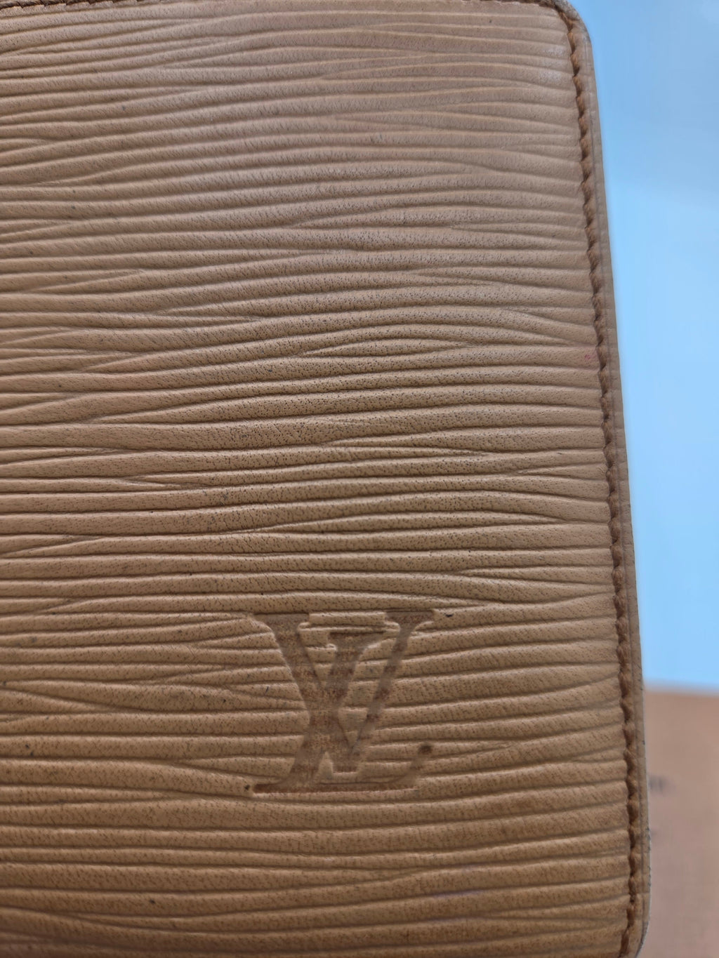 Close-up of a beige textured leather wallet or clutch with vertical grain and an embossed LV monogram on the front.