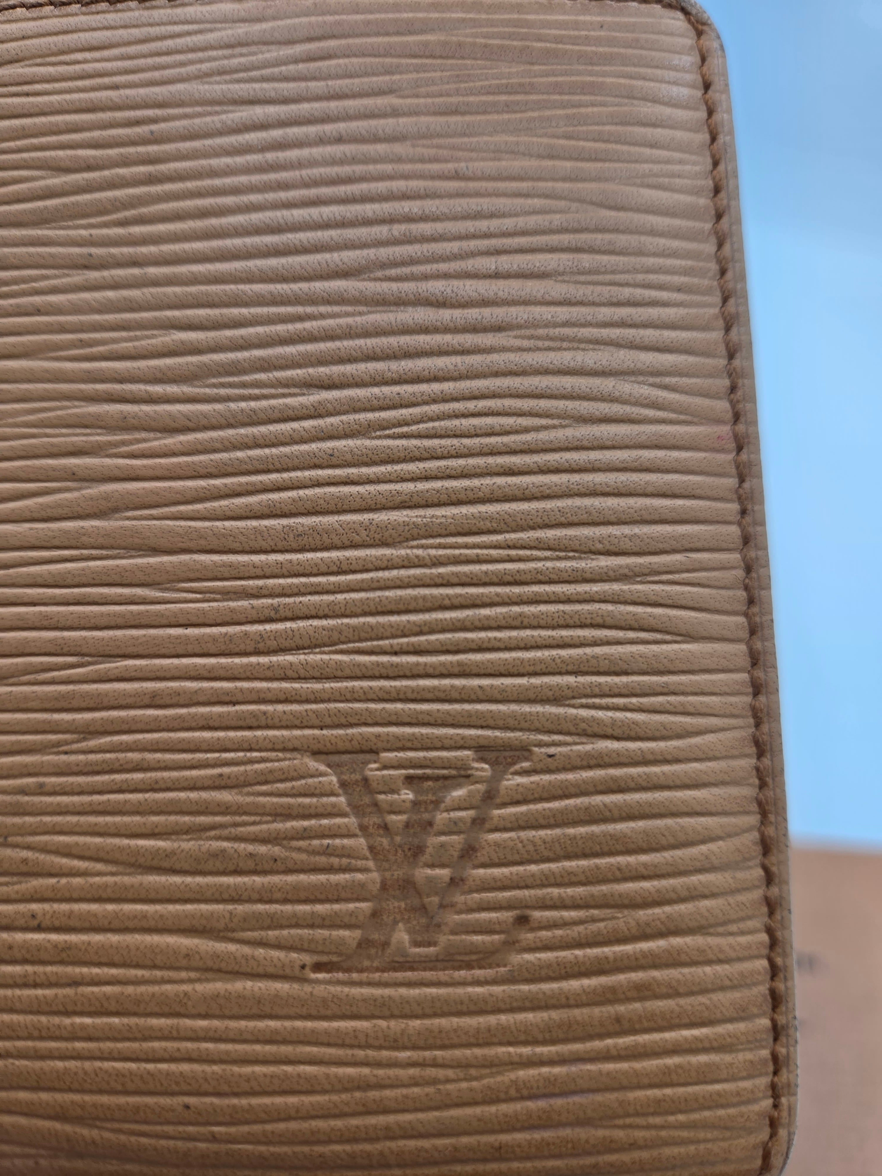 Close-up of a beige textured leather wallet or clutch with vertical grain and an embossed LV monogram on the front.