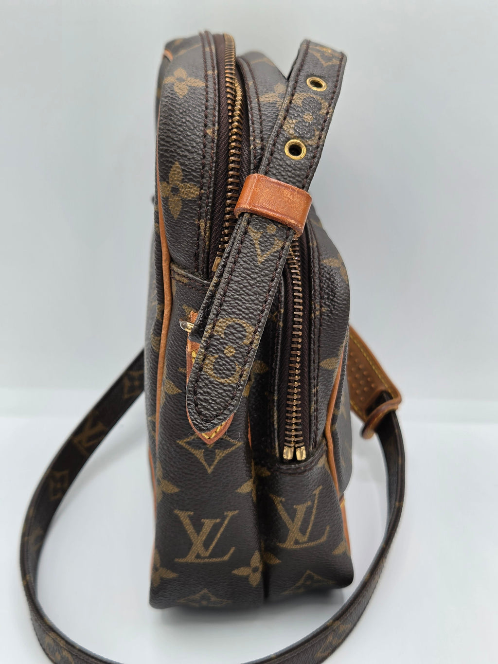 A Louis Vuitton monogram canvas shoulder bag in dark brown with tan leather trim and gold-tone zippers, shown against a plain light background.