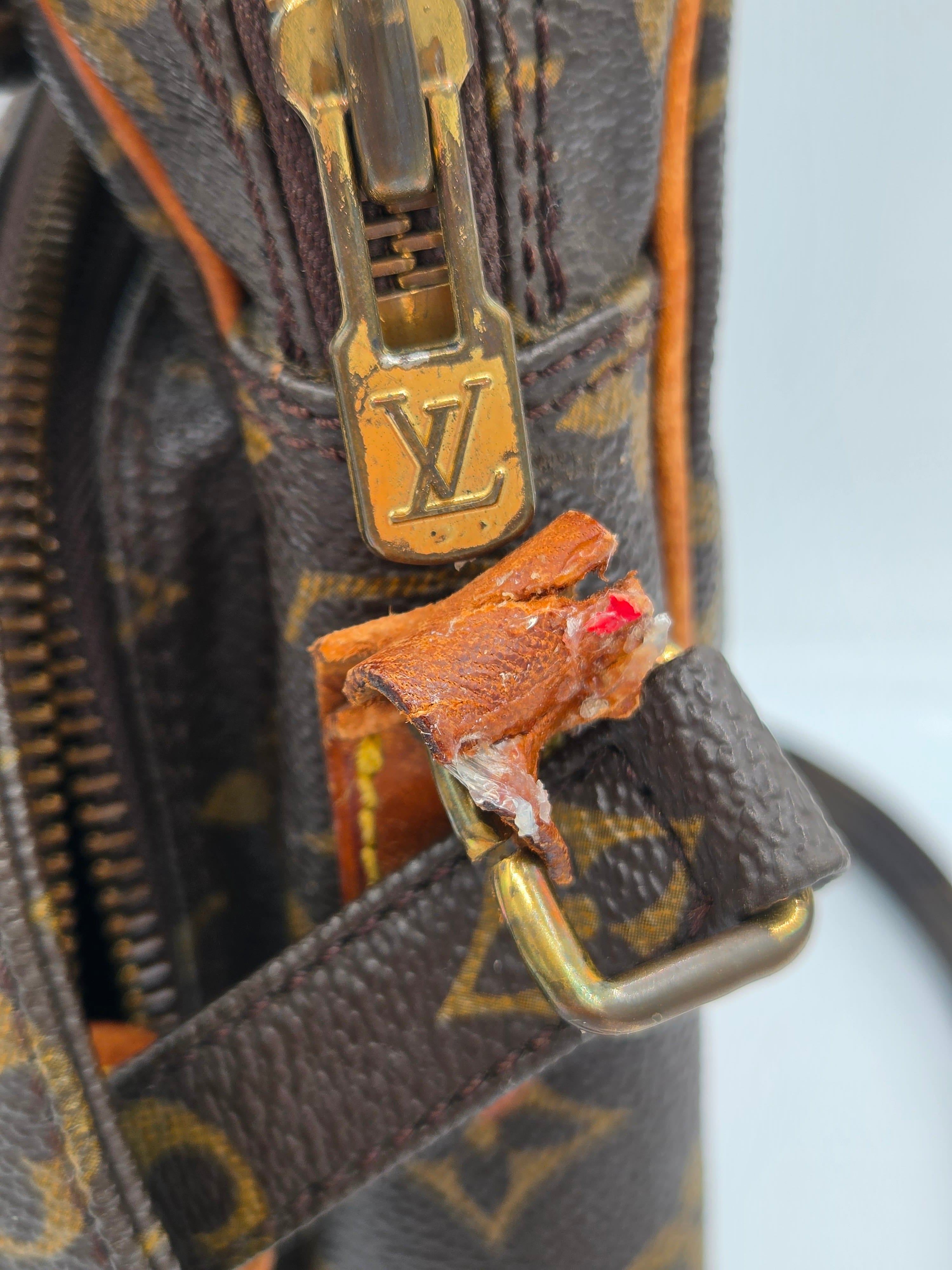 Close-up of a Louis Vuitton monogram handbag showing a damaged brown leather strap with exposed inner lining and a gold-tone metal zipper pull featuring the LV logo.