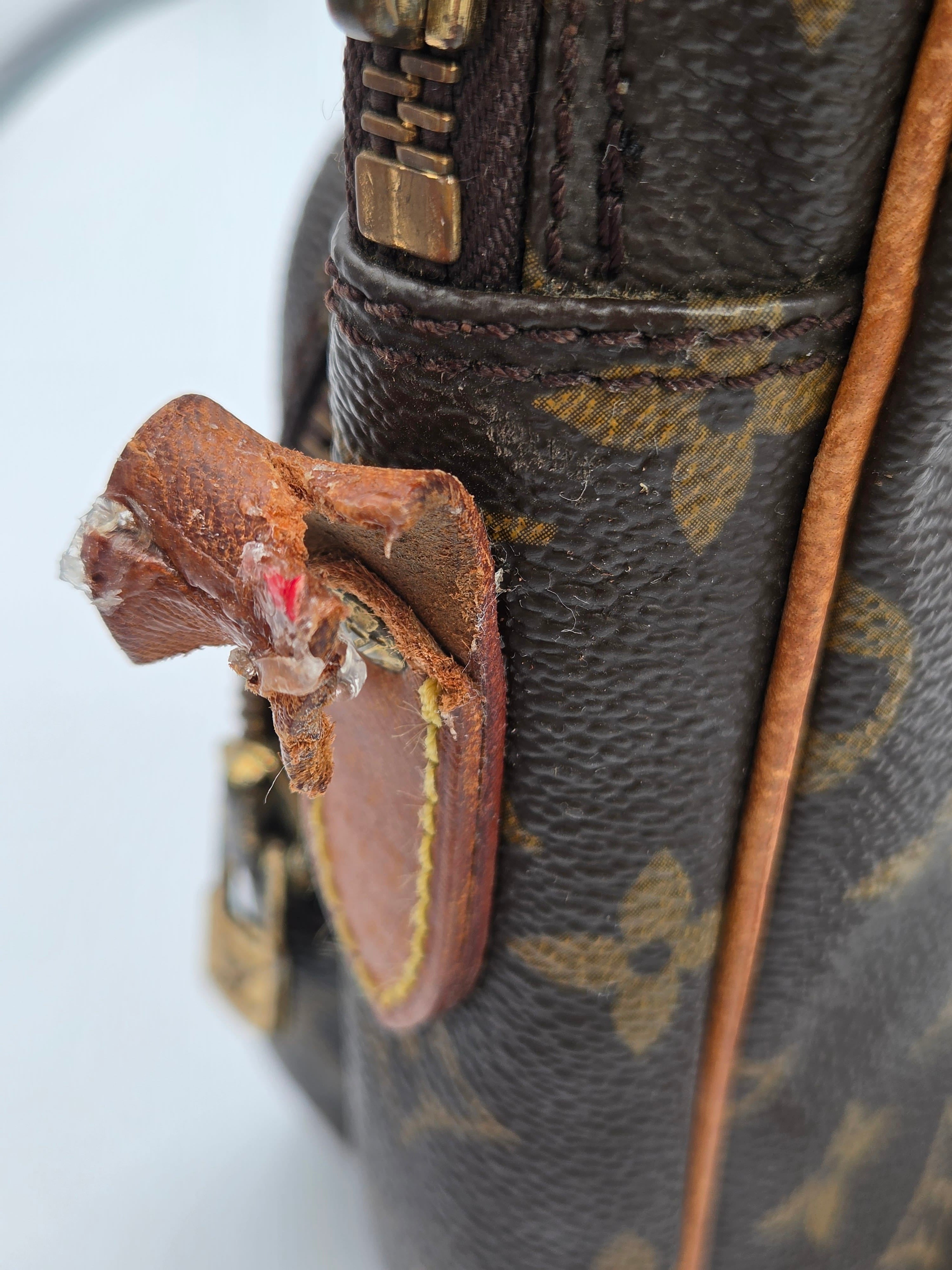 Close-up of a Louis Vuitton monogram handbag showing significant wear and tear on the brown leather strap attachment, with frayed and damaged edges.