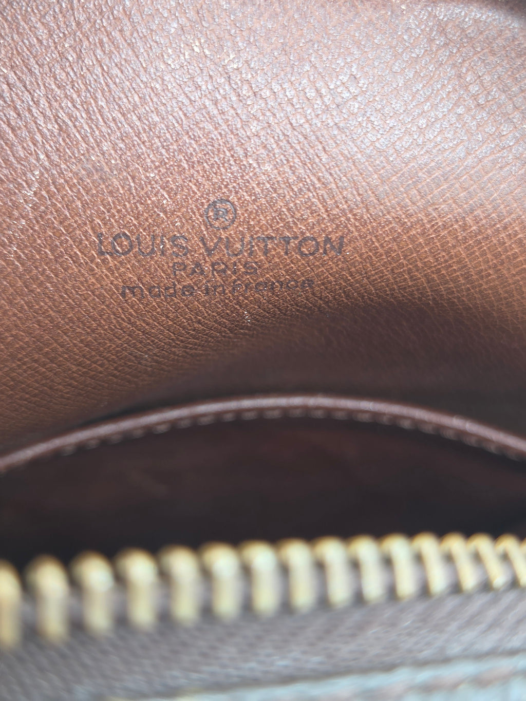 Close-up of a brown textured leather interior with embossed Louis Vuitton branding and a gold-toned zipper.