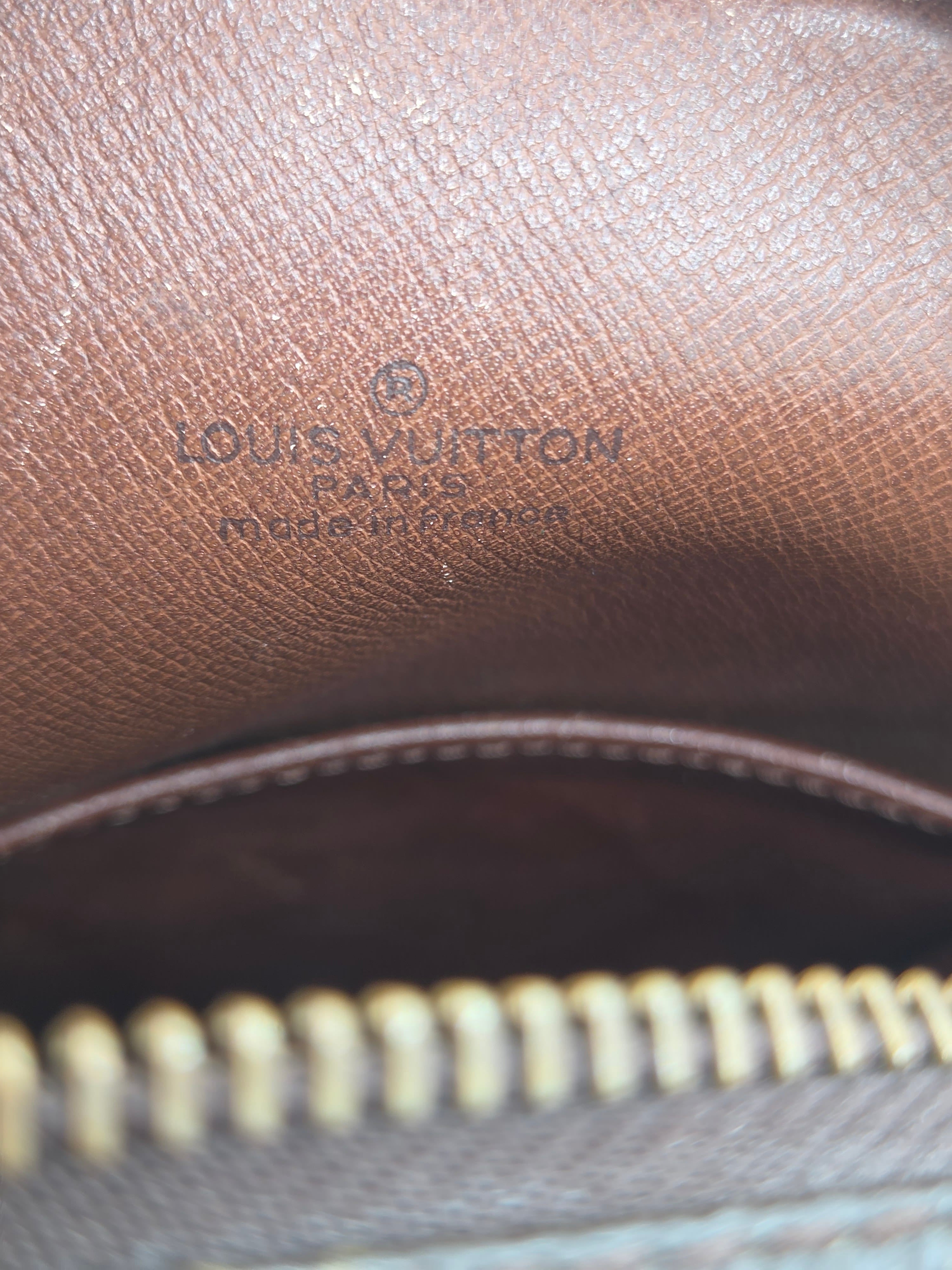 Close-up of a brown textured leather interior with embossed Louis Vuitton branding and a gold-toned zipper.