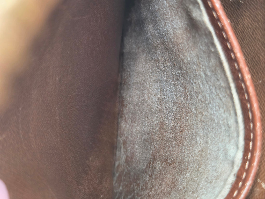 Close-up of the interior lining of a brown leather or canvas bag, showing a textured gray suede-like insert with brown stitched edge.