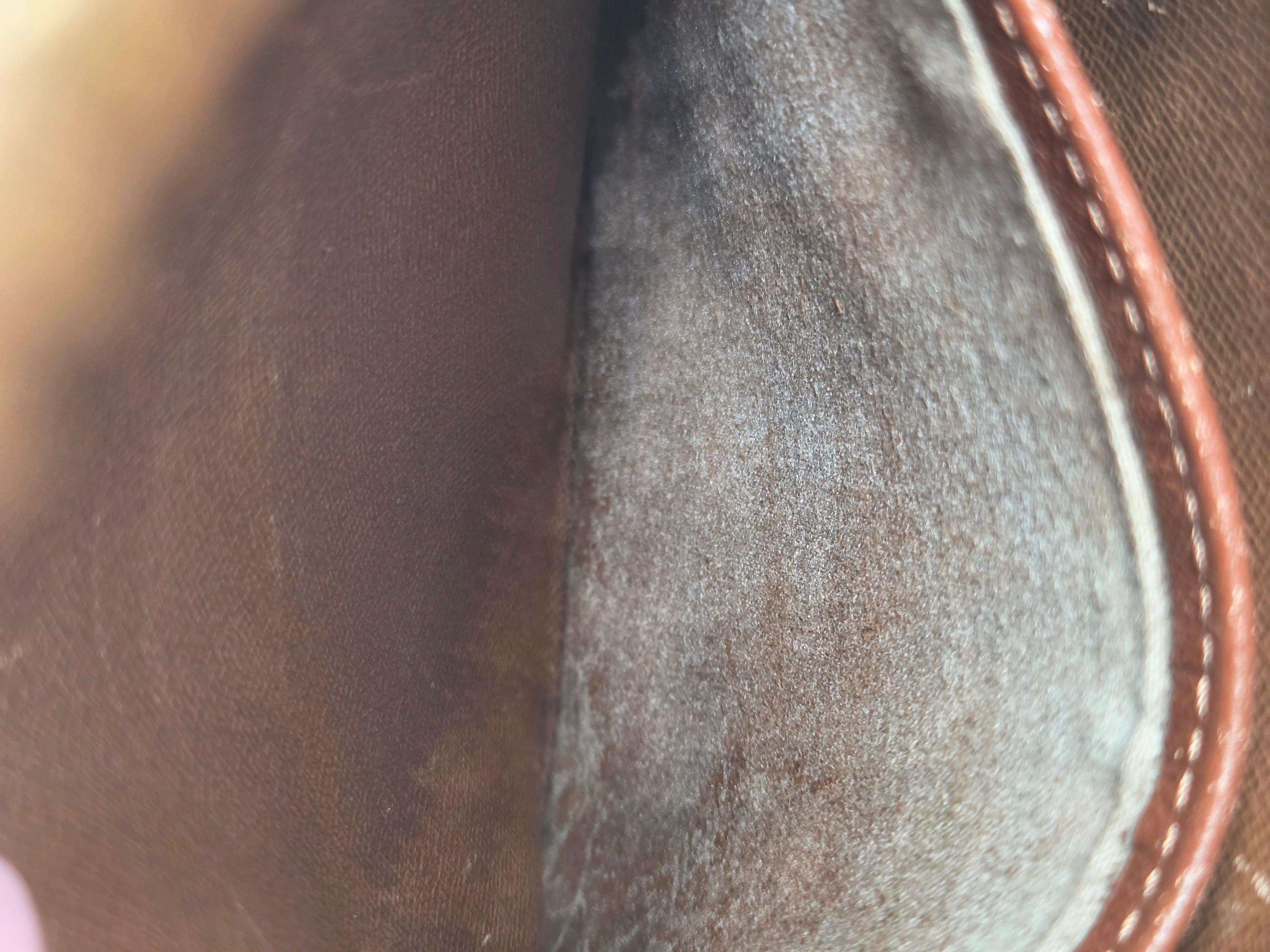 Close-up of the interior lining of a brown leather or canvas bag, showing a textured gray suede-like insert with brown stitched edge.