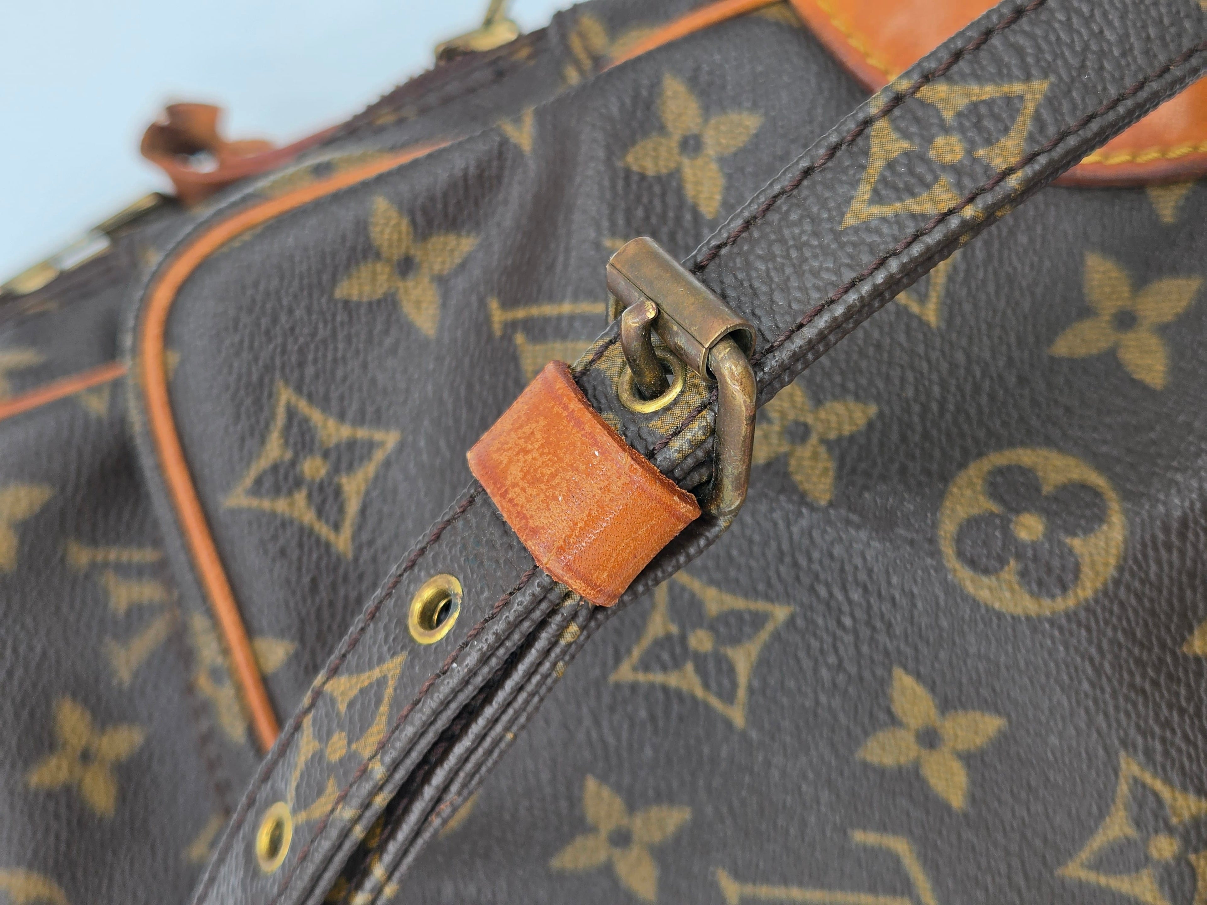 Close-up of a Louis Vuitton monogram canvas bag with dark brown coated canvas, tan leather trim, brass-tone hardware, and a shoulder strap.