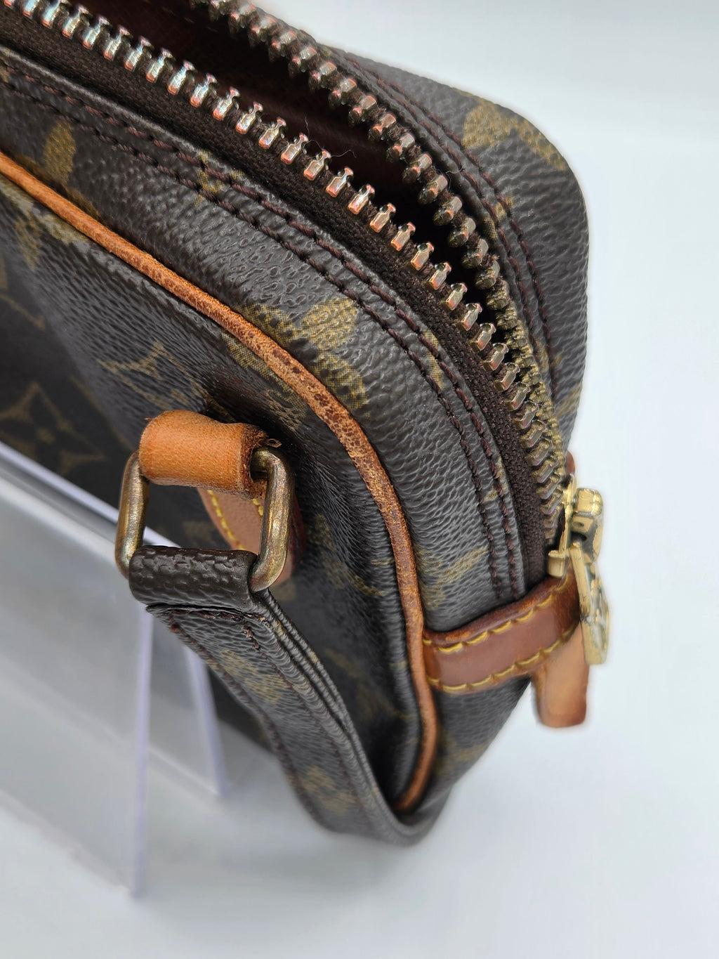 Close-up of a Louis Vuitton monogram canvas pouch with brown leather trim and gold-tone hardware on a white background.