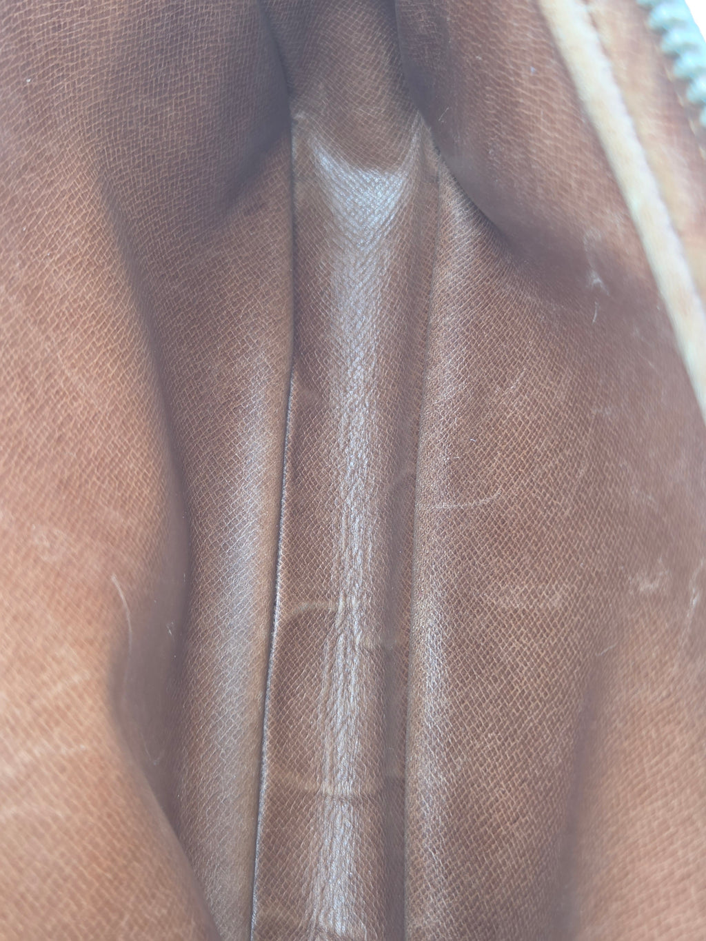 Close-up of a brown textured leather or faux-leather material with visible creases and a light-colored zipper edge at the top.