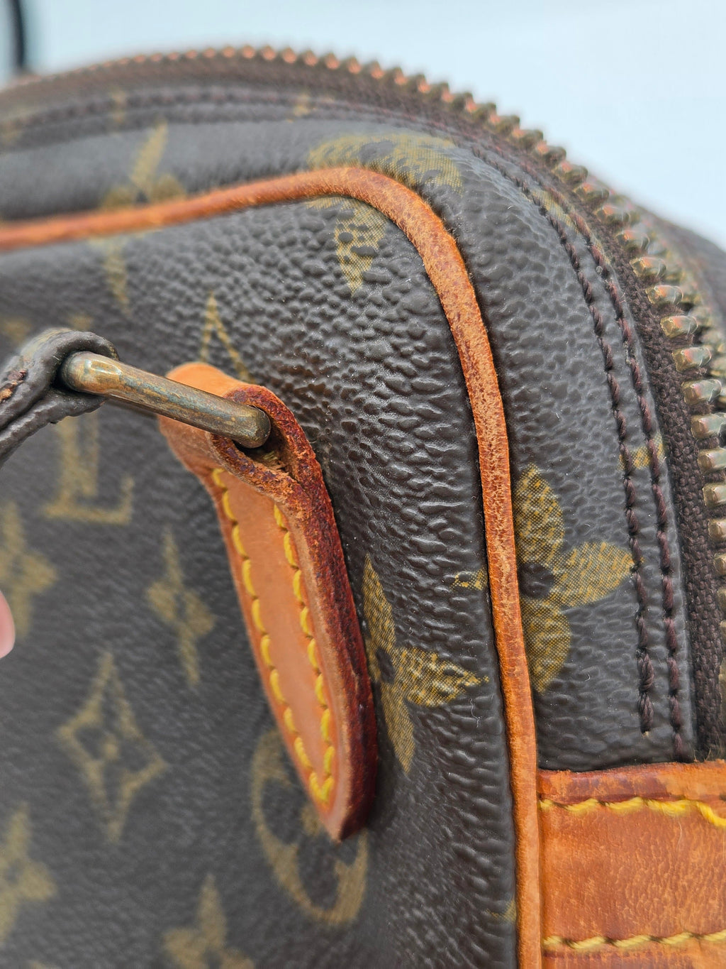Close-up of a Louis Vuitton monogram canvas bag with tan leather trim and a metal zipper pull.