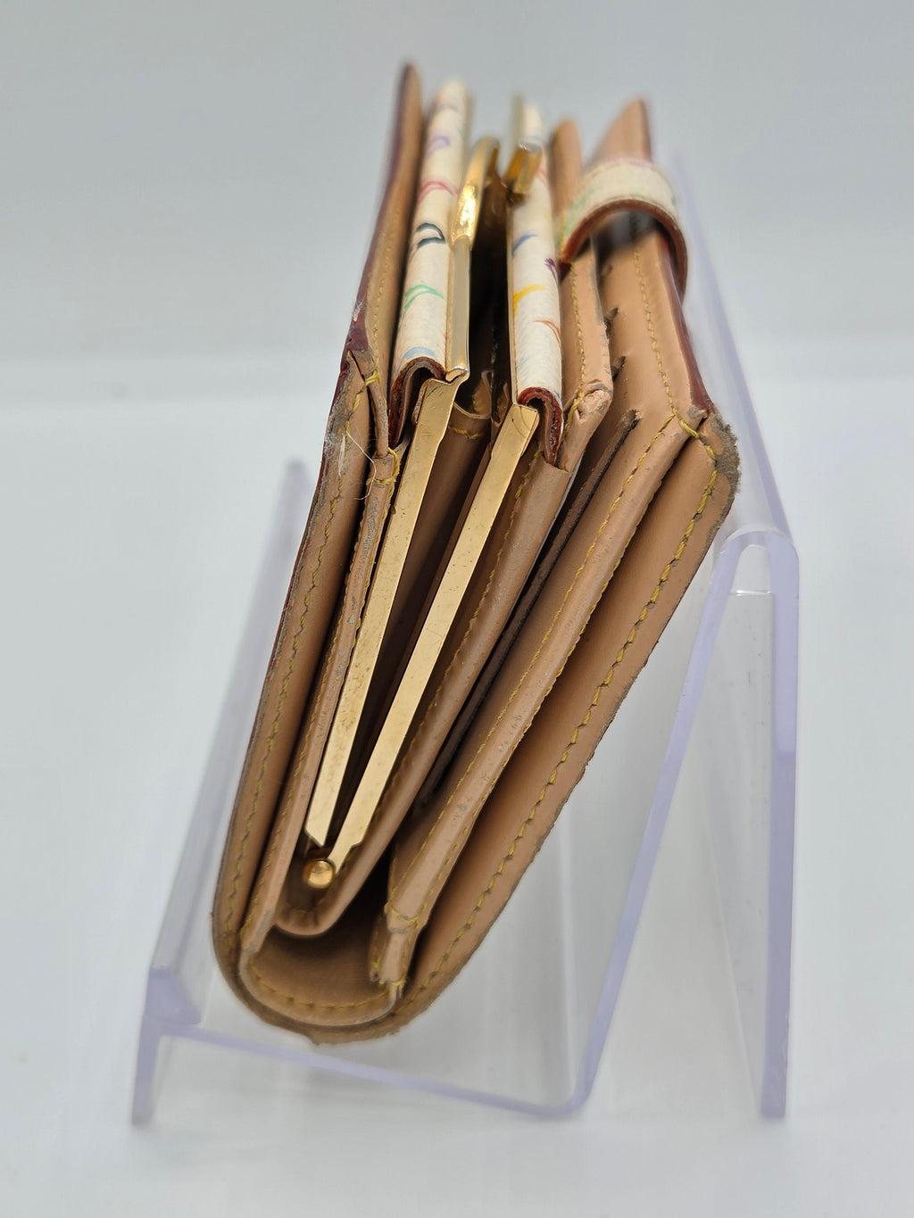 A tan leather wallet with multiple card slots and decorative patterned paper inserts, displayed on a clear acrylic stand against a white background.